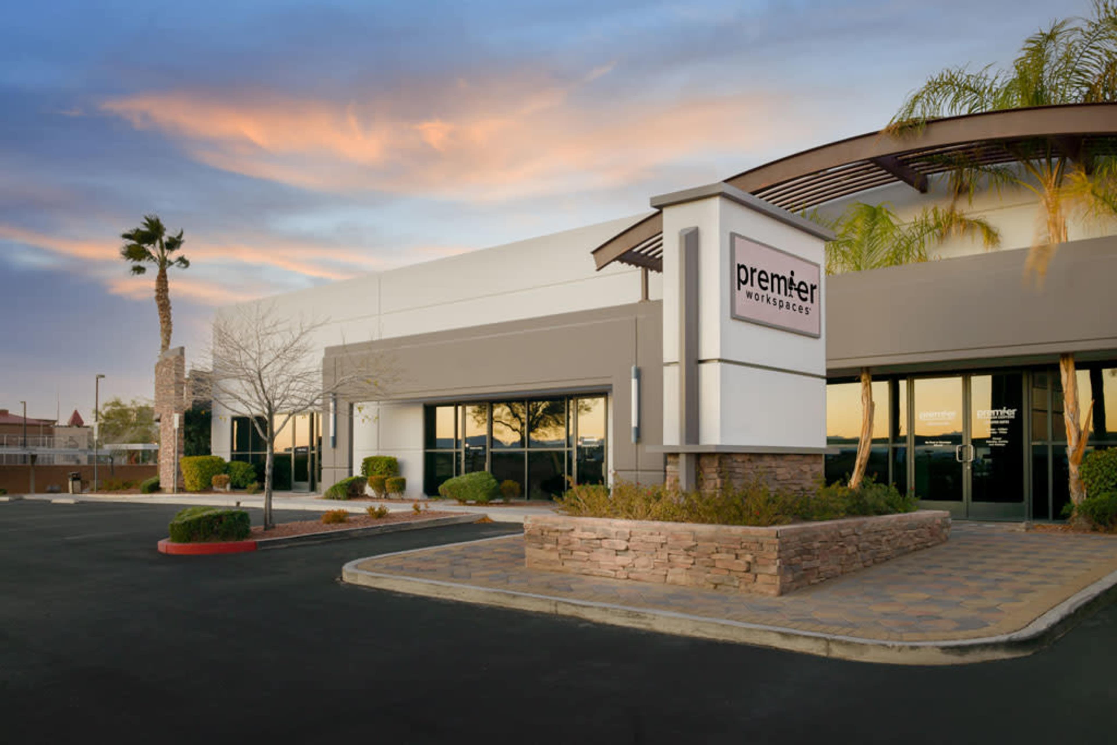 A modern commercial building with a sign for "premier" and landscaped surroundings under a colorful sky at dusk.