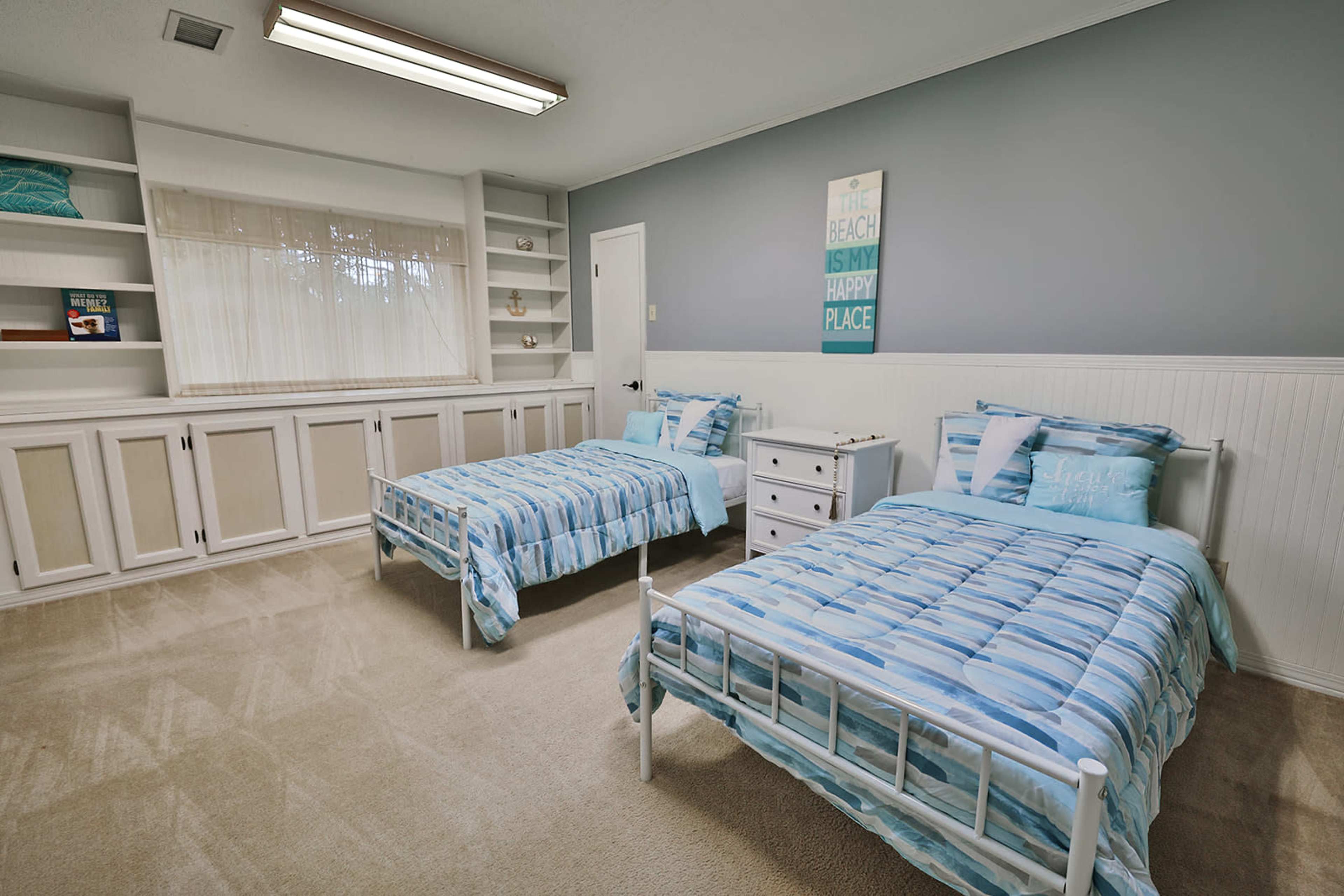 A room with two twin beds covered in blue striped bedding, a white nightstand, and a shelf built into the wall.
