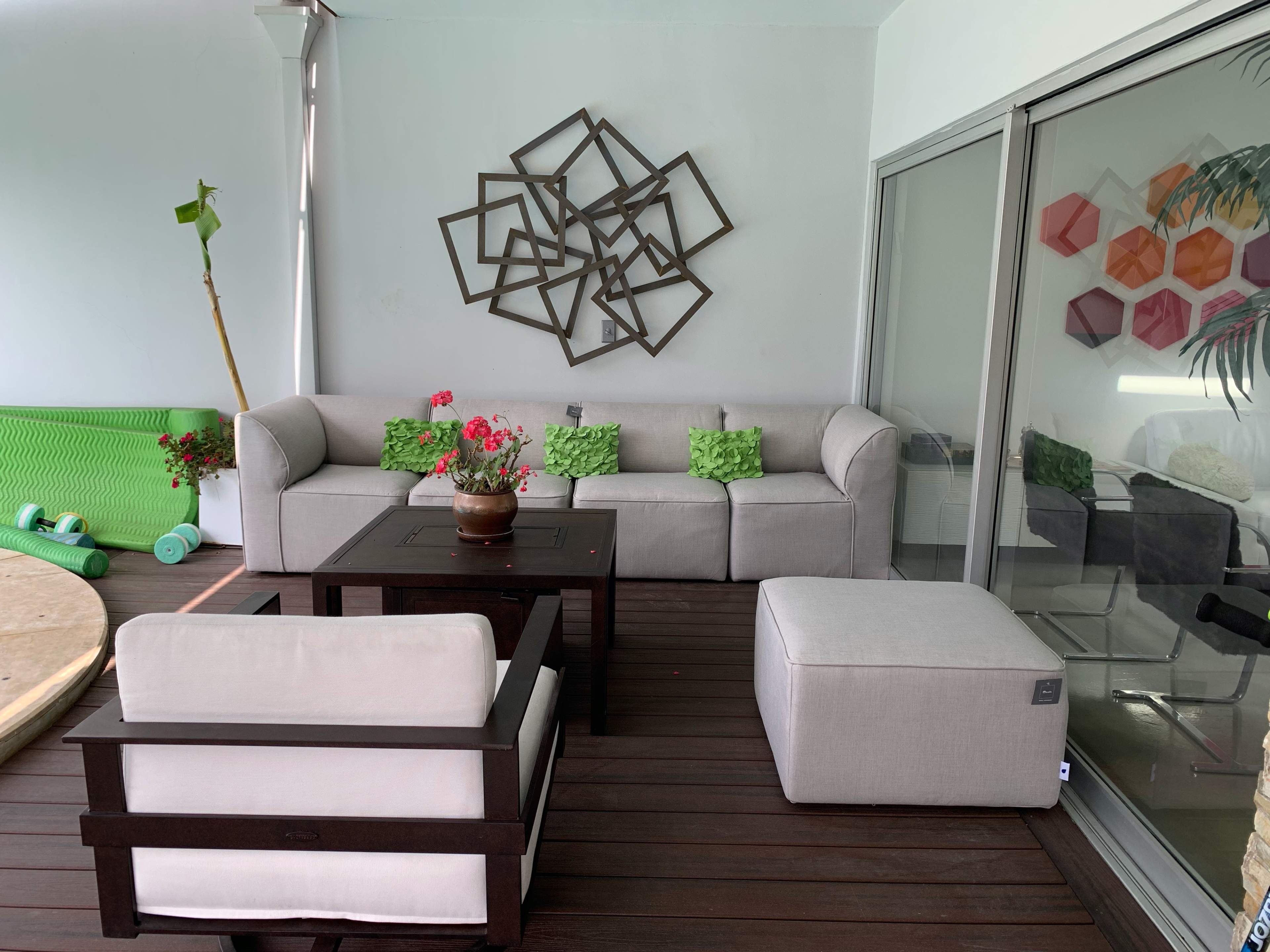 The image shows a patio area with a gray sofa, a wooden coffee table, and a light-colored armchair, all arranged on a wooden floor next to sliding glass doors.