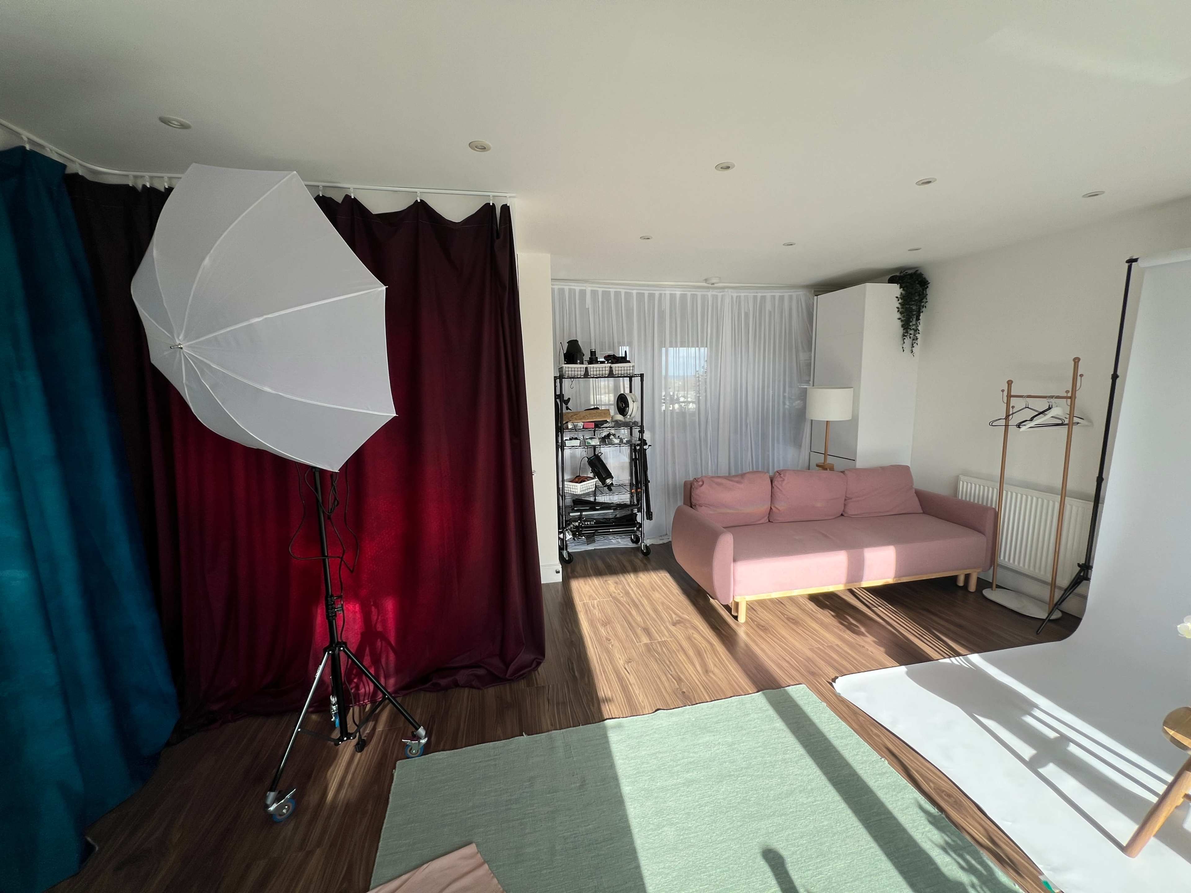 The image shows a photography studio with a pink sofa, backdrop curtains, and lighting equipment.