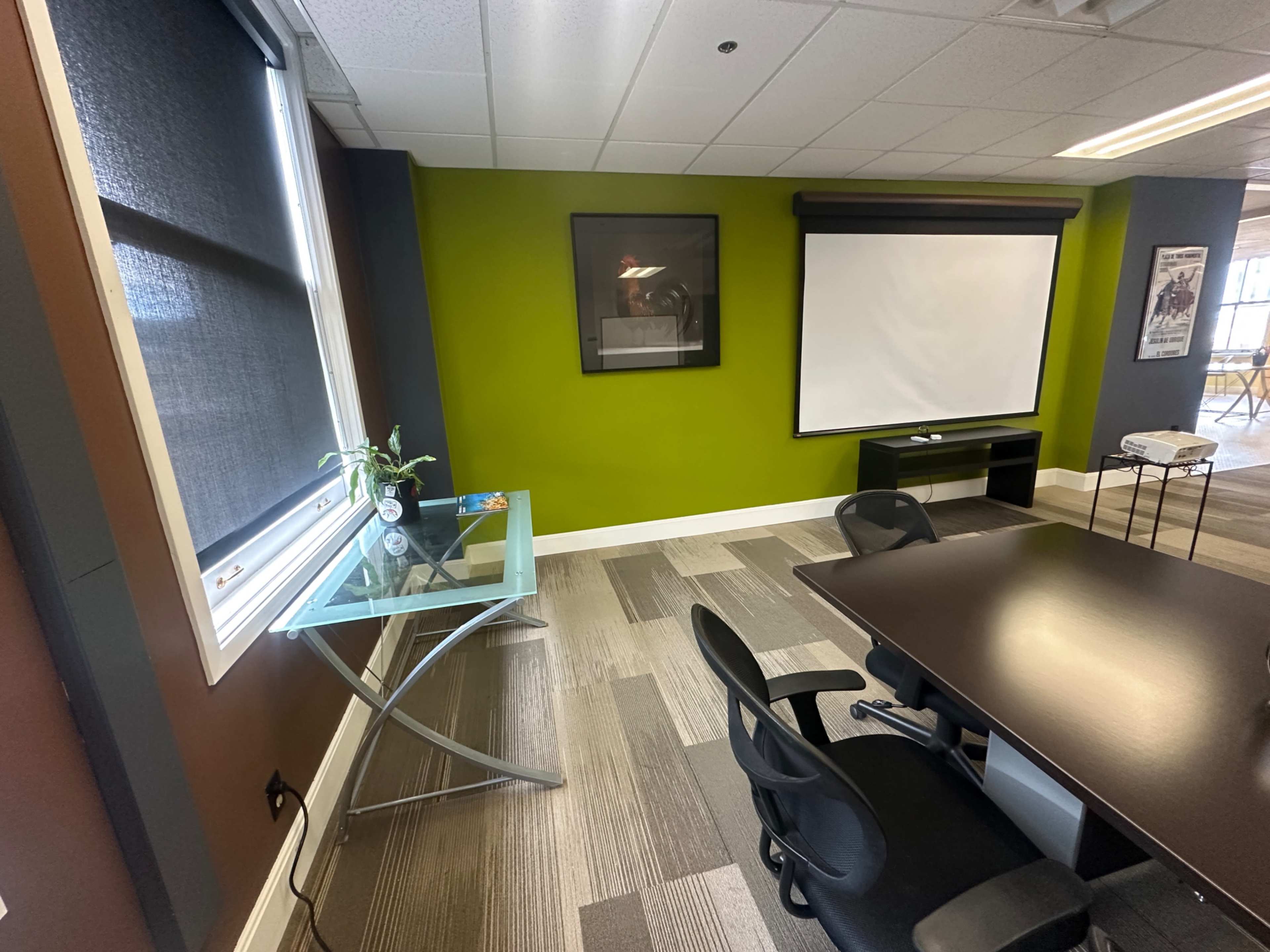 The image shows a modern conference room with a green accent wall, a large screen for presentations, a glass table, and ergonomic chairs around a dark conference table.