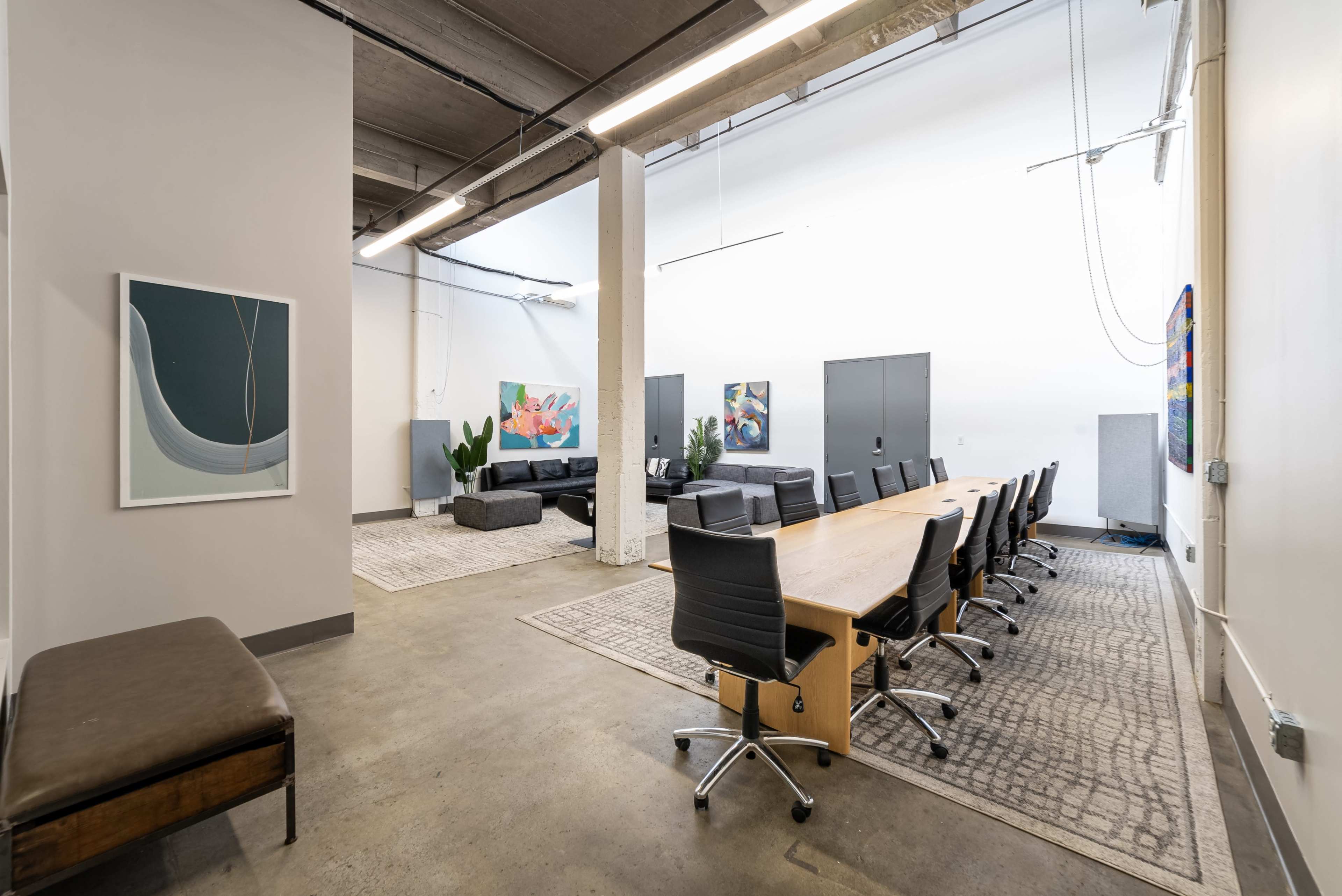 A modern office space featuring a long wooden conference table surrounded by black chairs, with a lounge area and artwork on the walls.