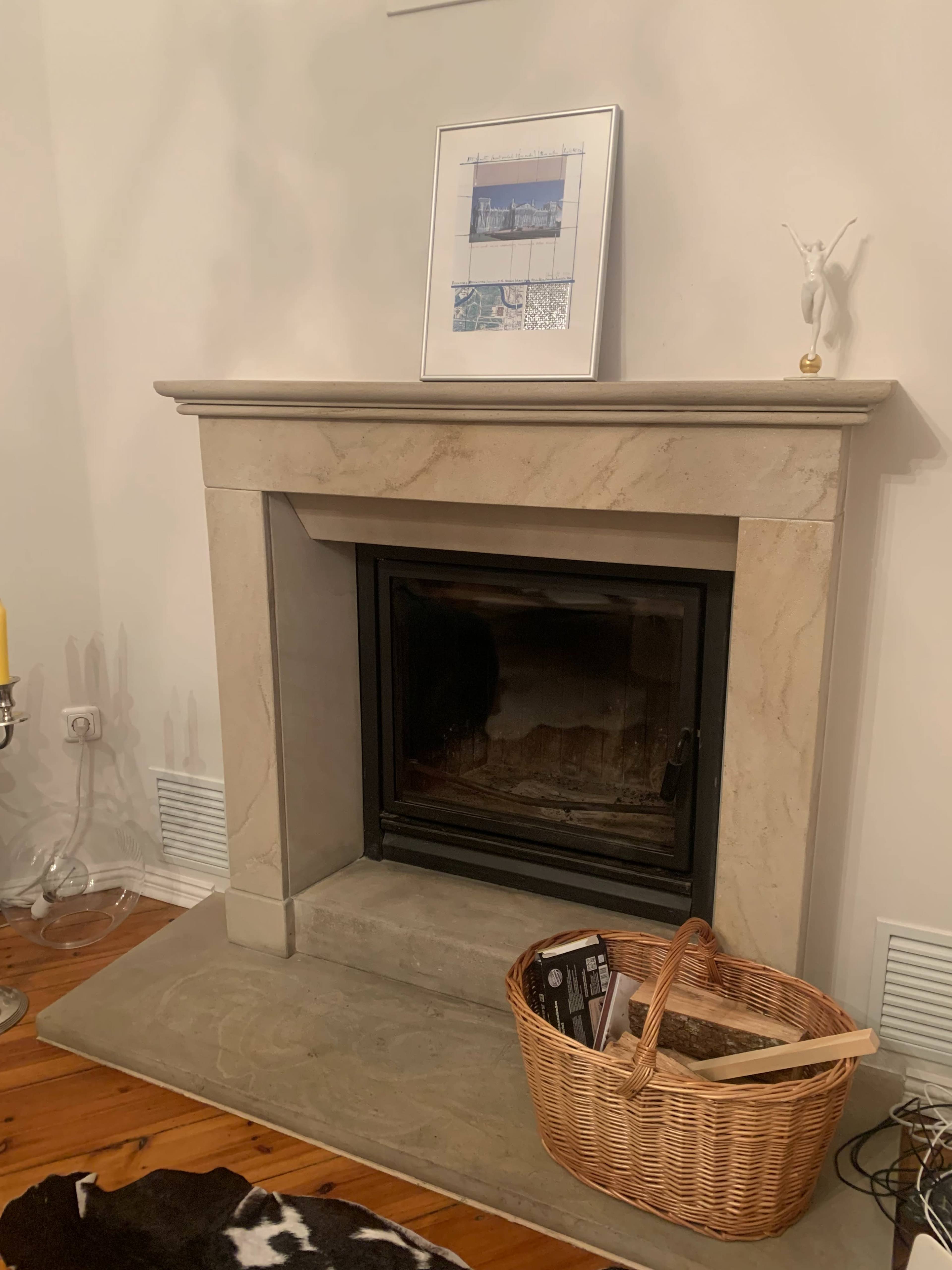 A stone fireplace with a framed picture above it and a woven basket on the floor beside it.