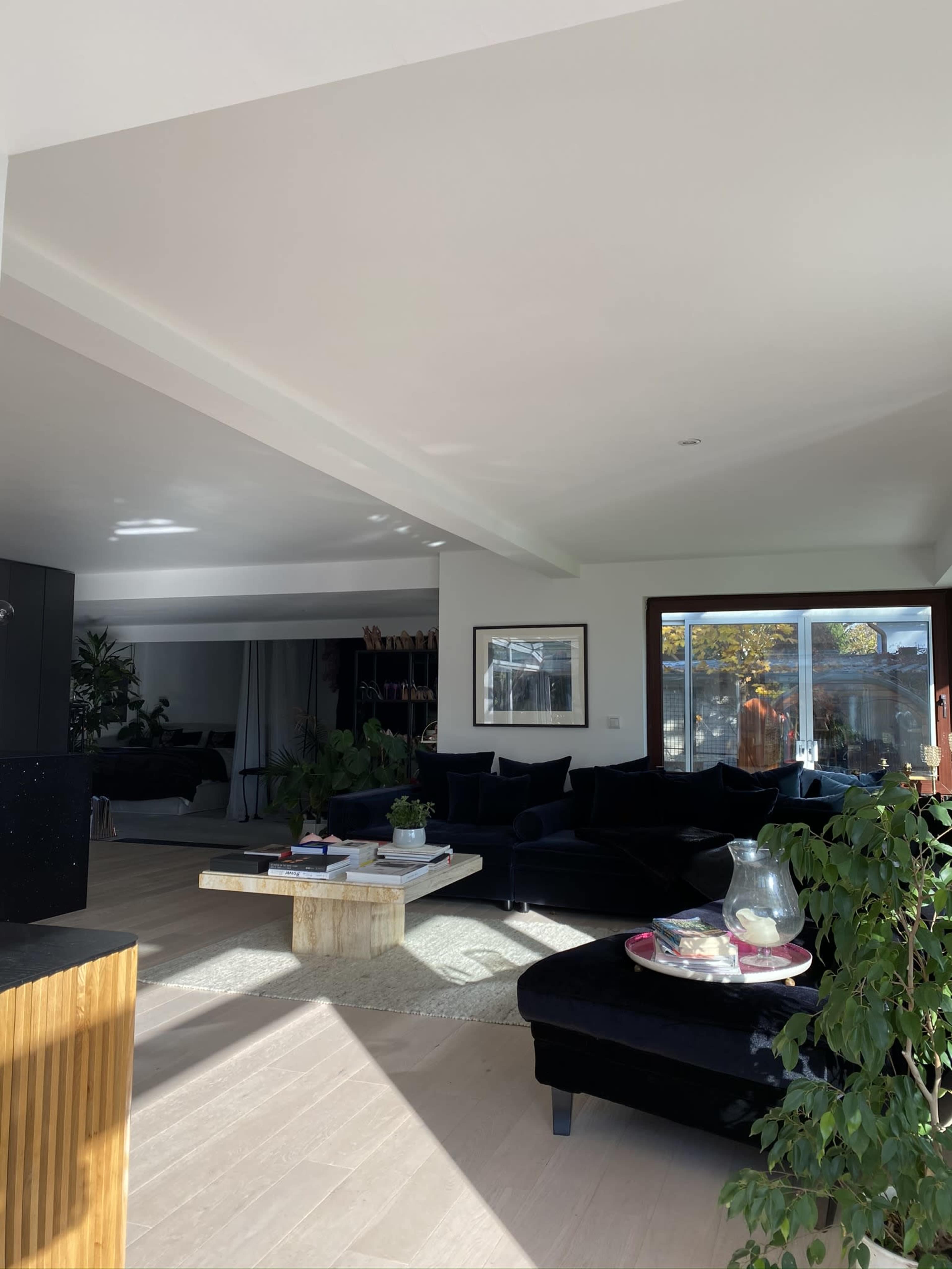 A spacious modern living room with black furniture, a wooden coffee table, and large windows allowing natural light to illuminate the space.