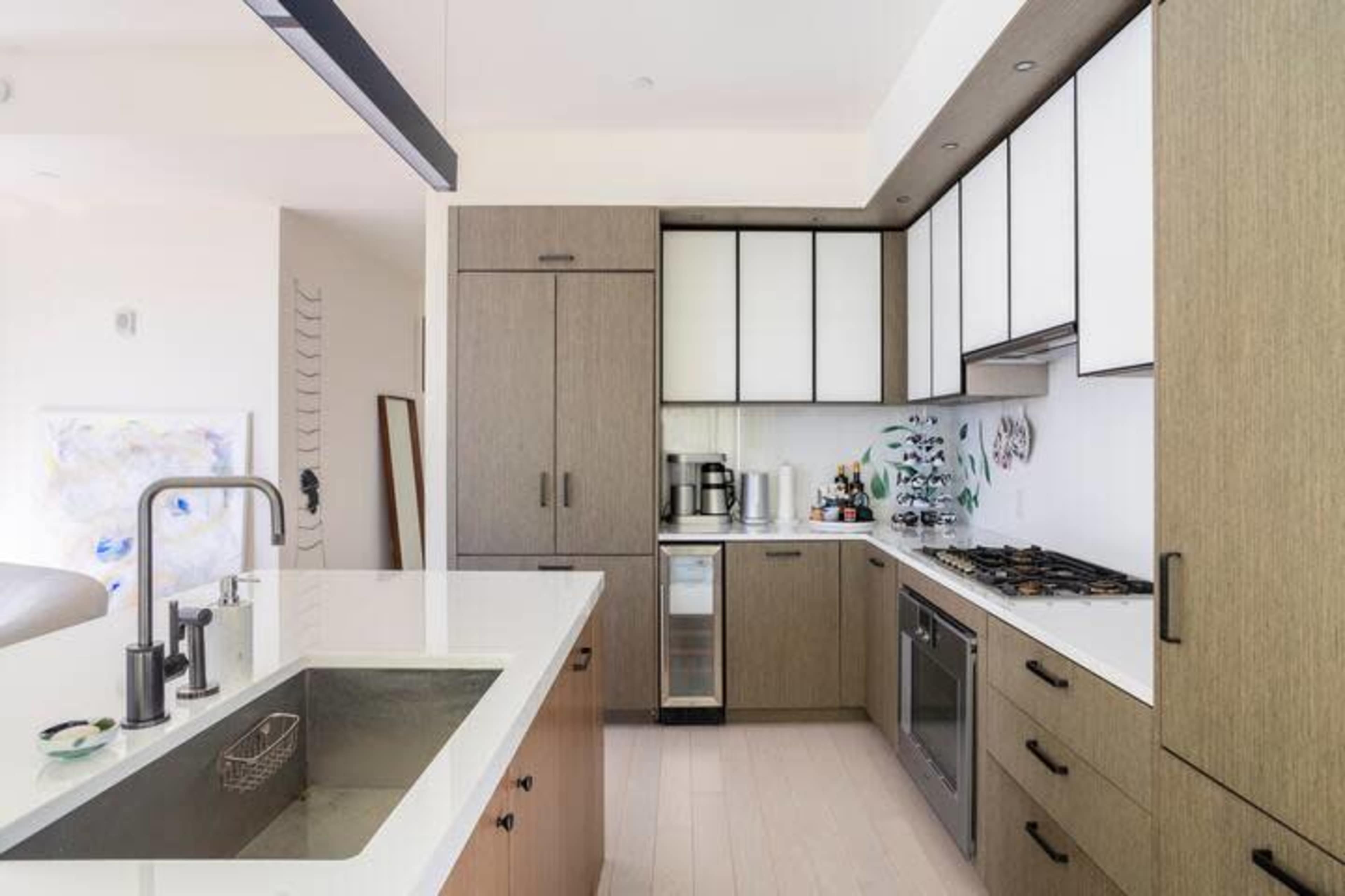 The image shows a modern kitchen featuring wooden cabinetry, white countertops, and a stainless steel appliance setup.