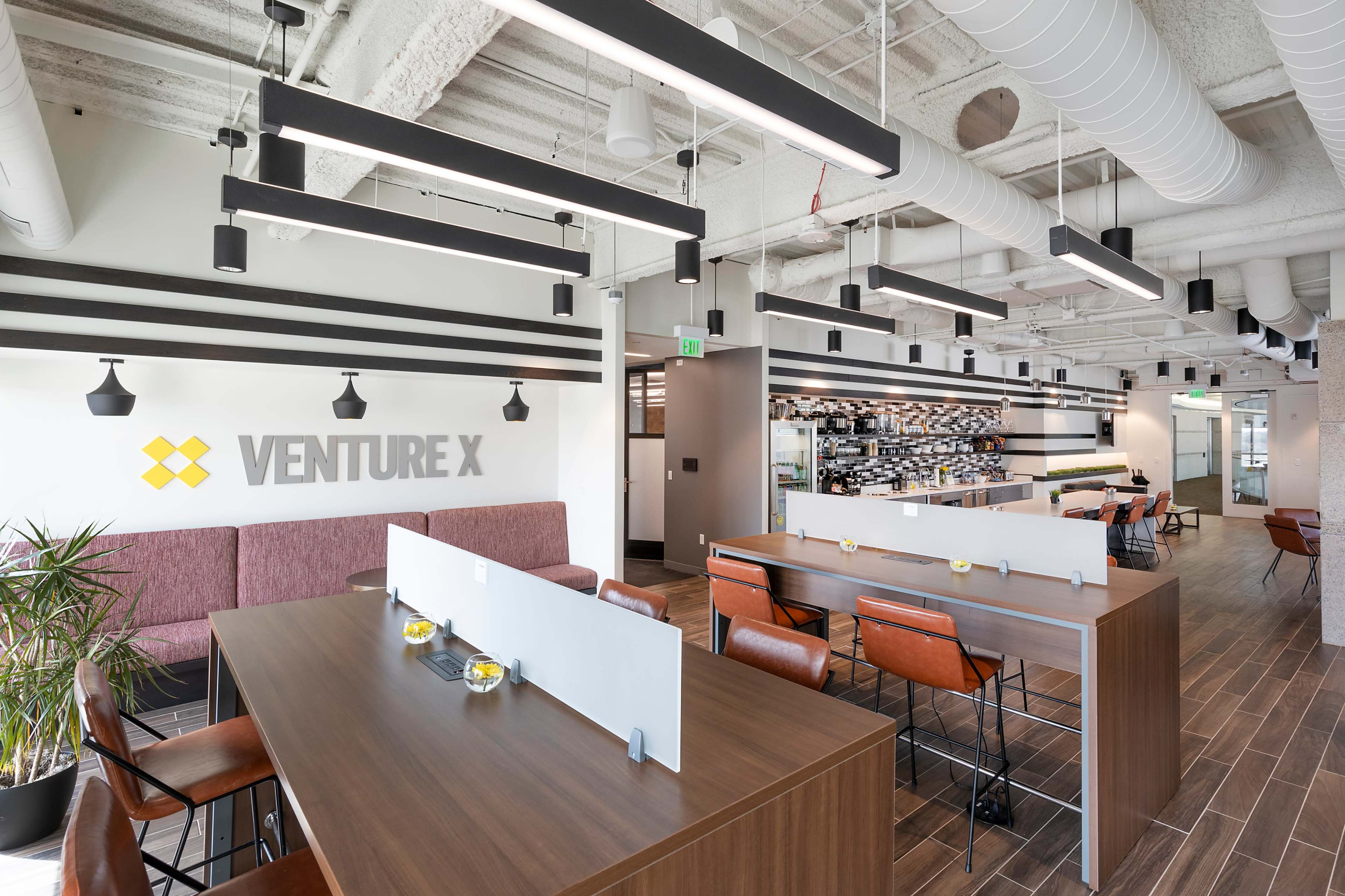 A modern coworking space with a seating area, tables for work, and a coffee bar in the background.