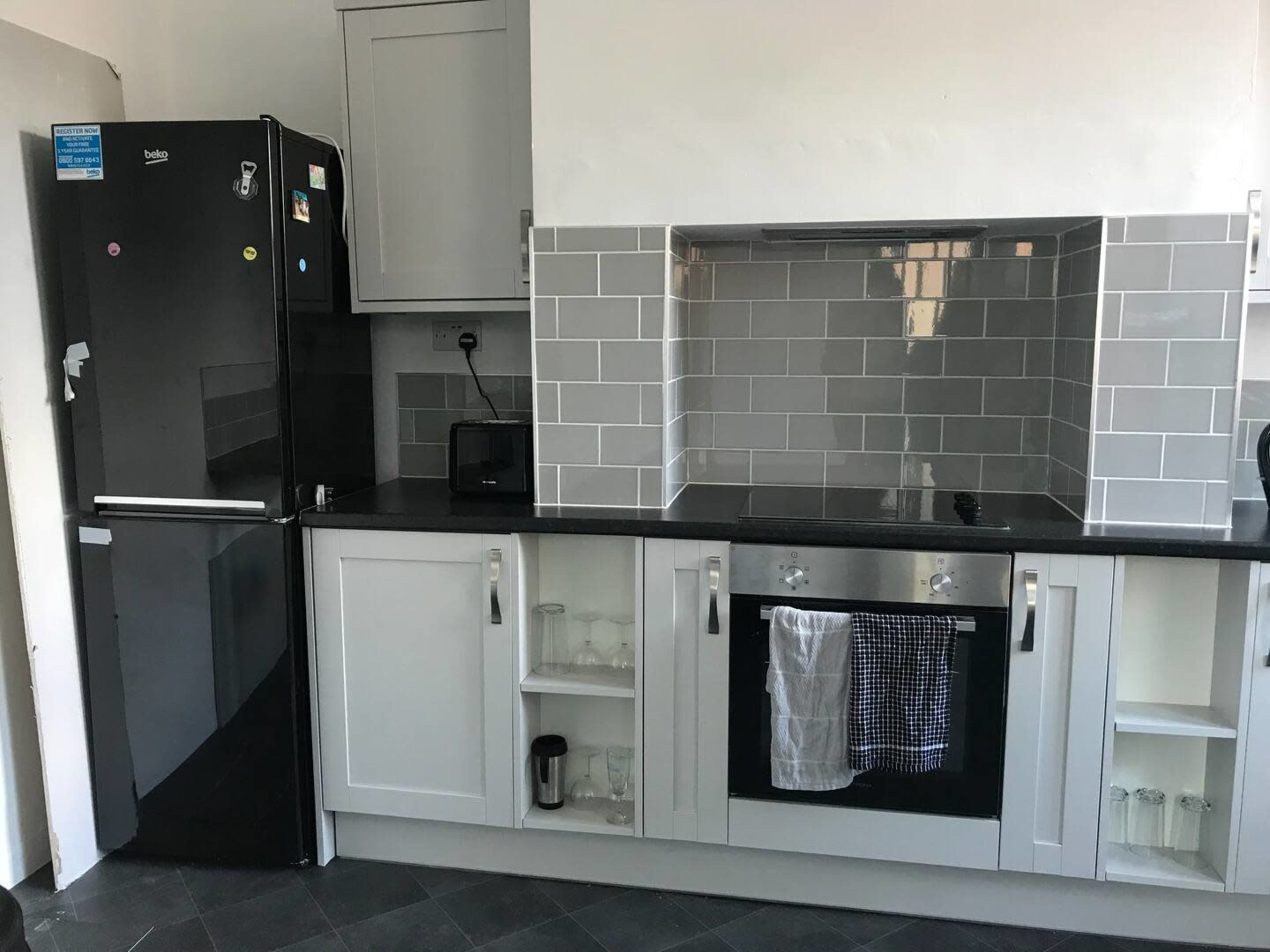 A modern kitchen with a black refrigerator, a countertop oven, and gray tiled backsplash.