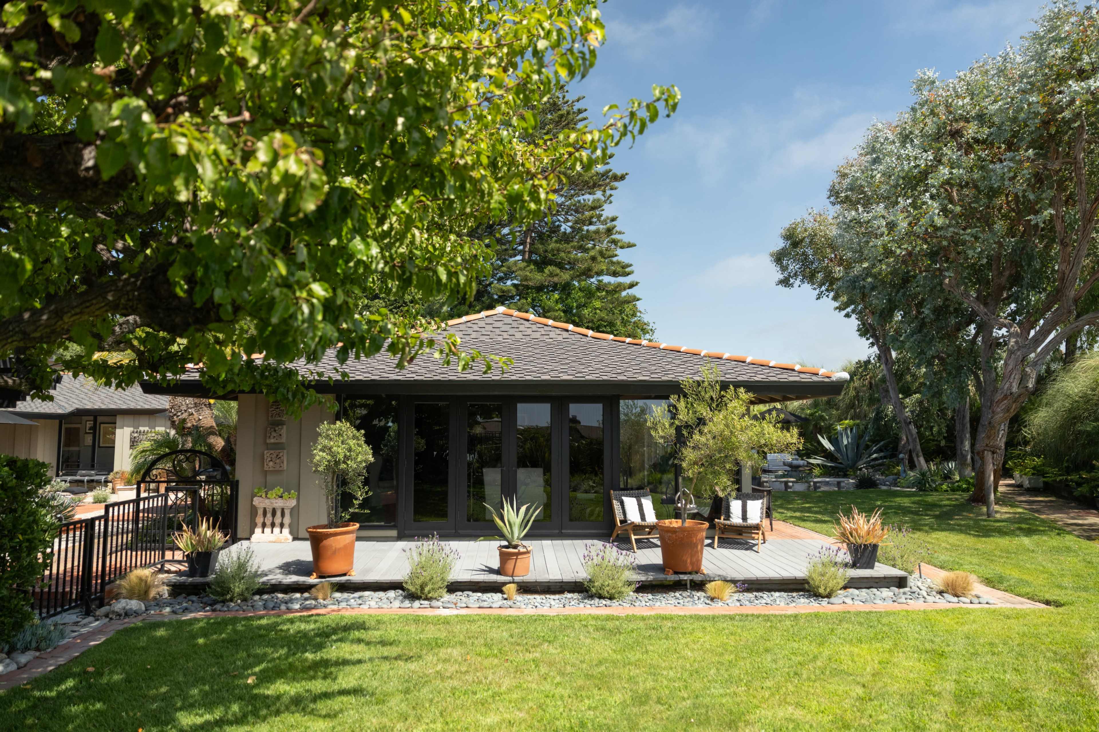 A modern house with a patio is surrounded by a well-maintained garden featuring various plants and trees.