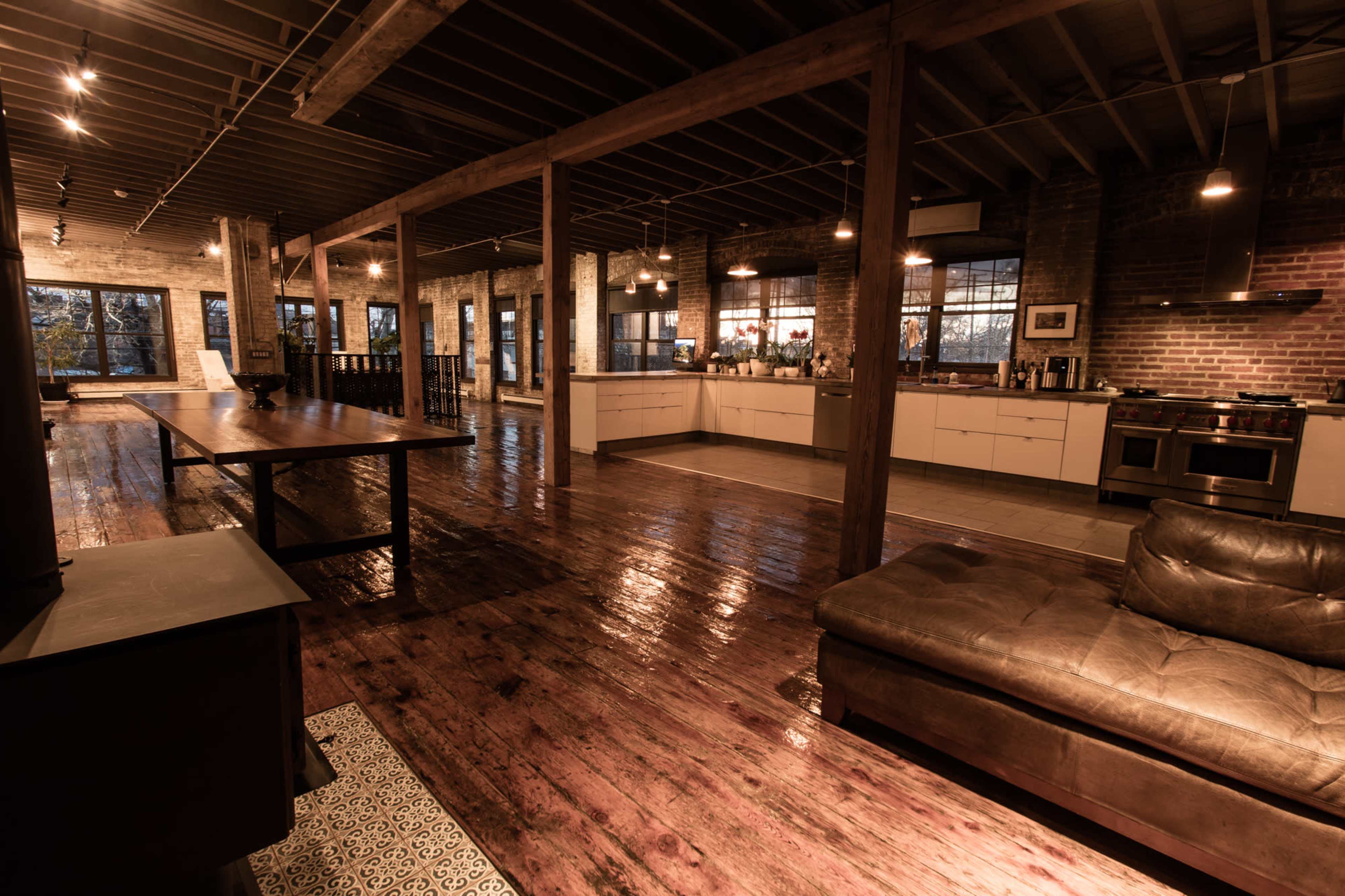 The spacious industrial-style kitchen and living area feature exposed brick walls, wooden beams, and polished hardwood floors.
