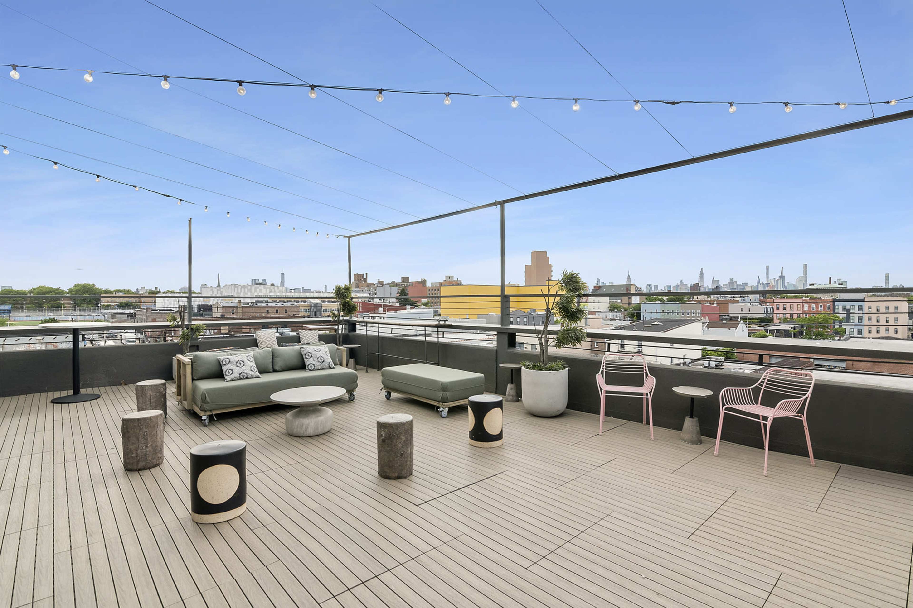 The image shows a rooftop terrace featuring modern seating, string lights, and a panoramic view of the city skyline.