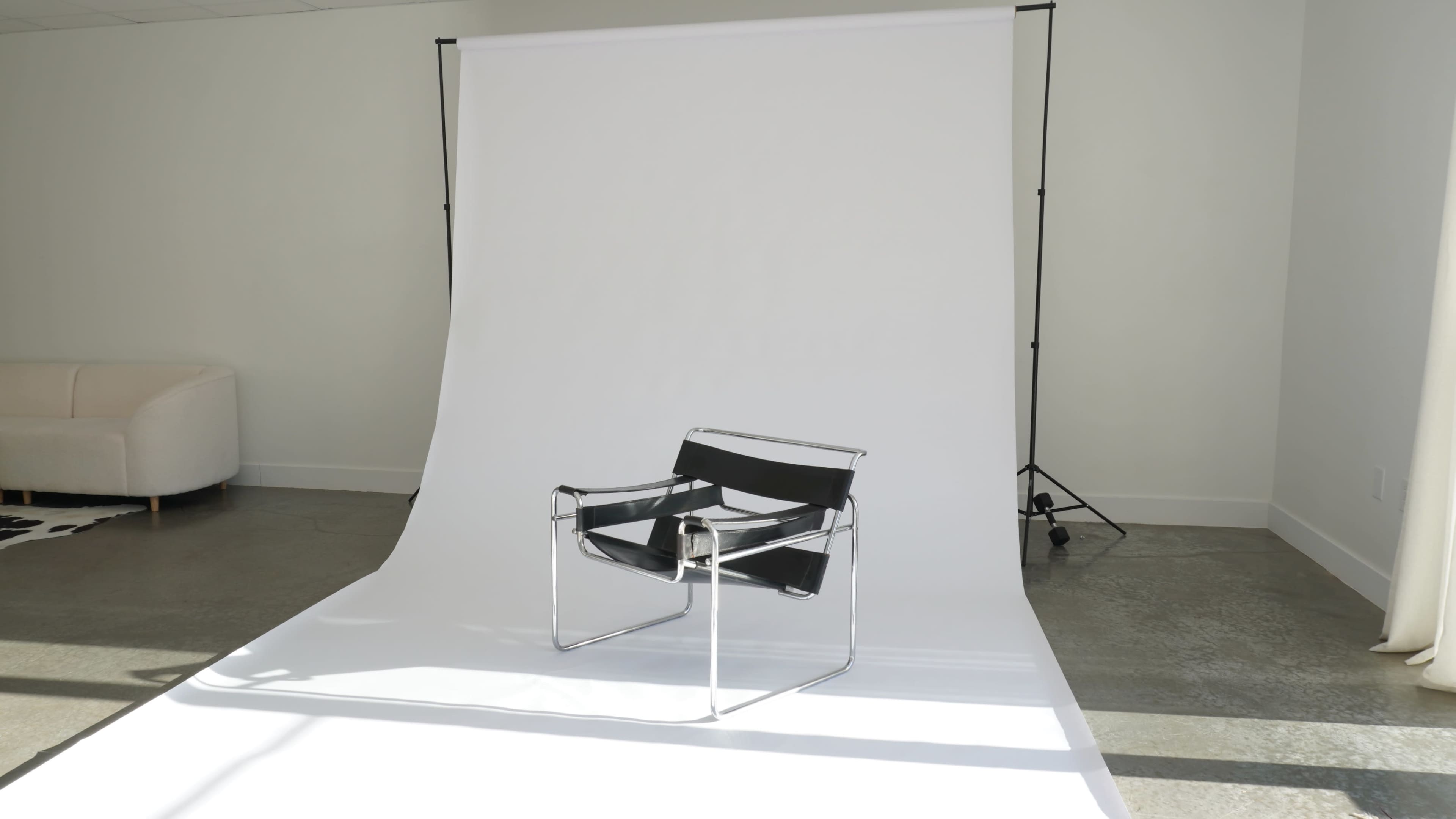 A modern black chair is positioned on a white backdrop in a well-lit room.