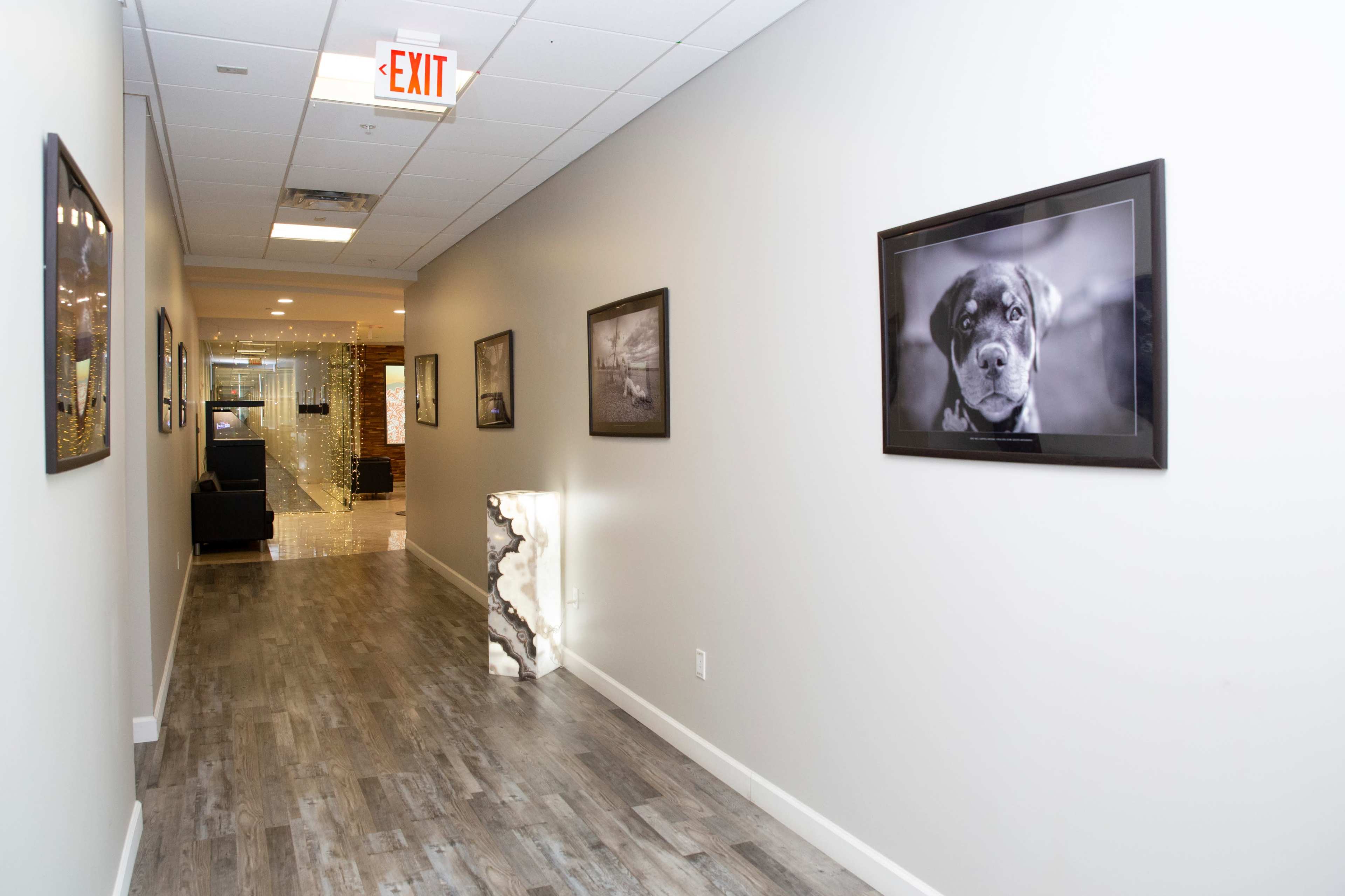 A well-lit hallway features framed black-and-white photographs on the walls, with a decorative light fixture and an exit sign at one end.