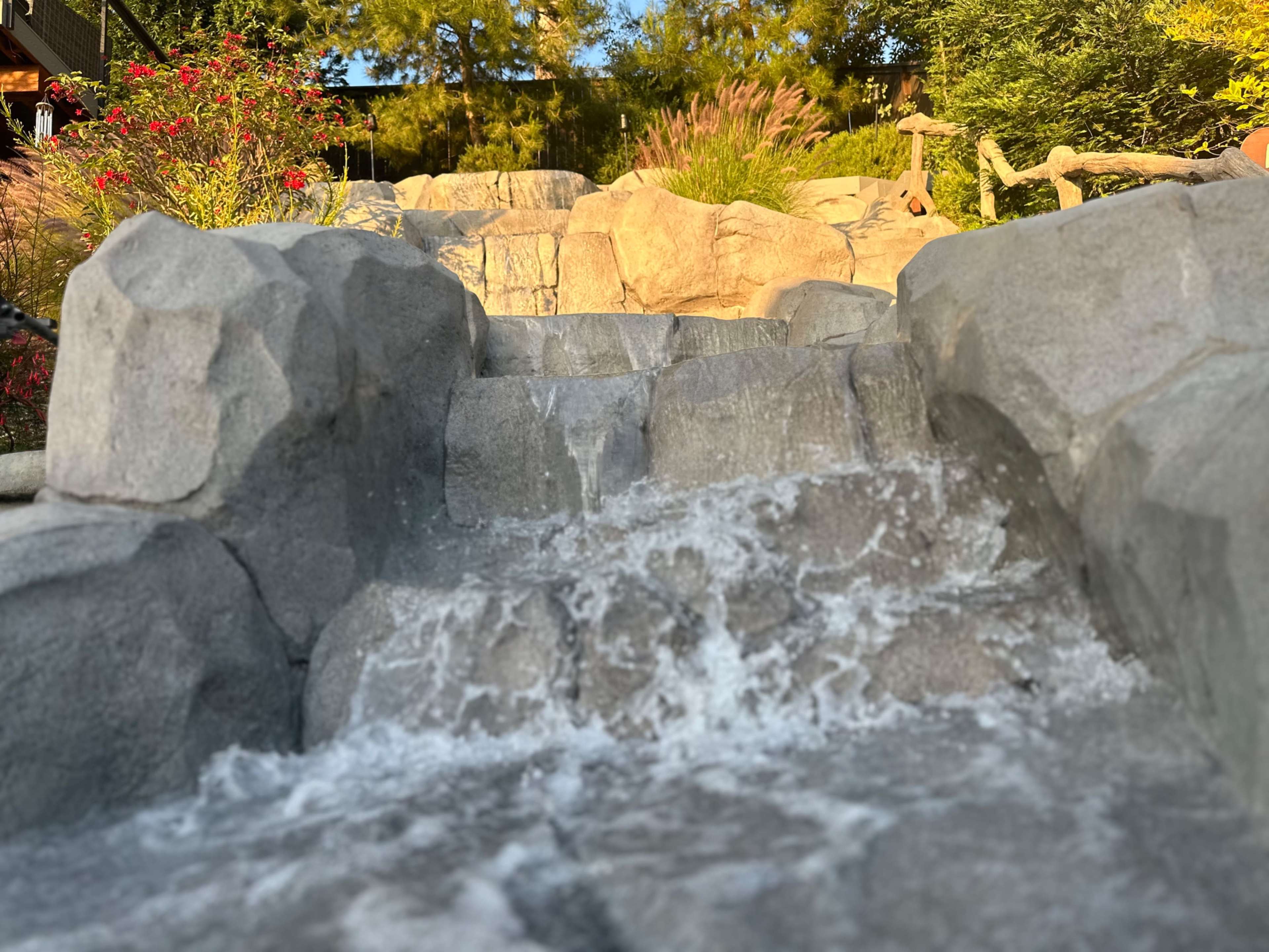 Water cascades down a rocky pathway surrounded by greenery and flowers.