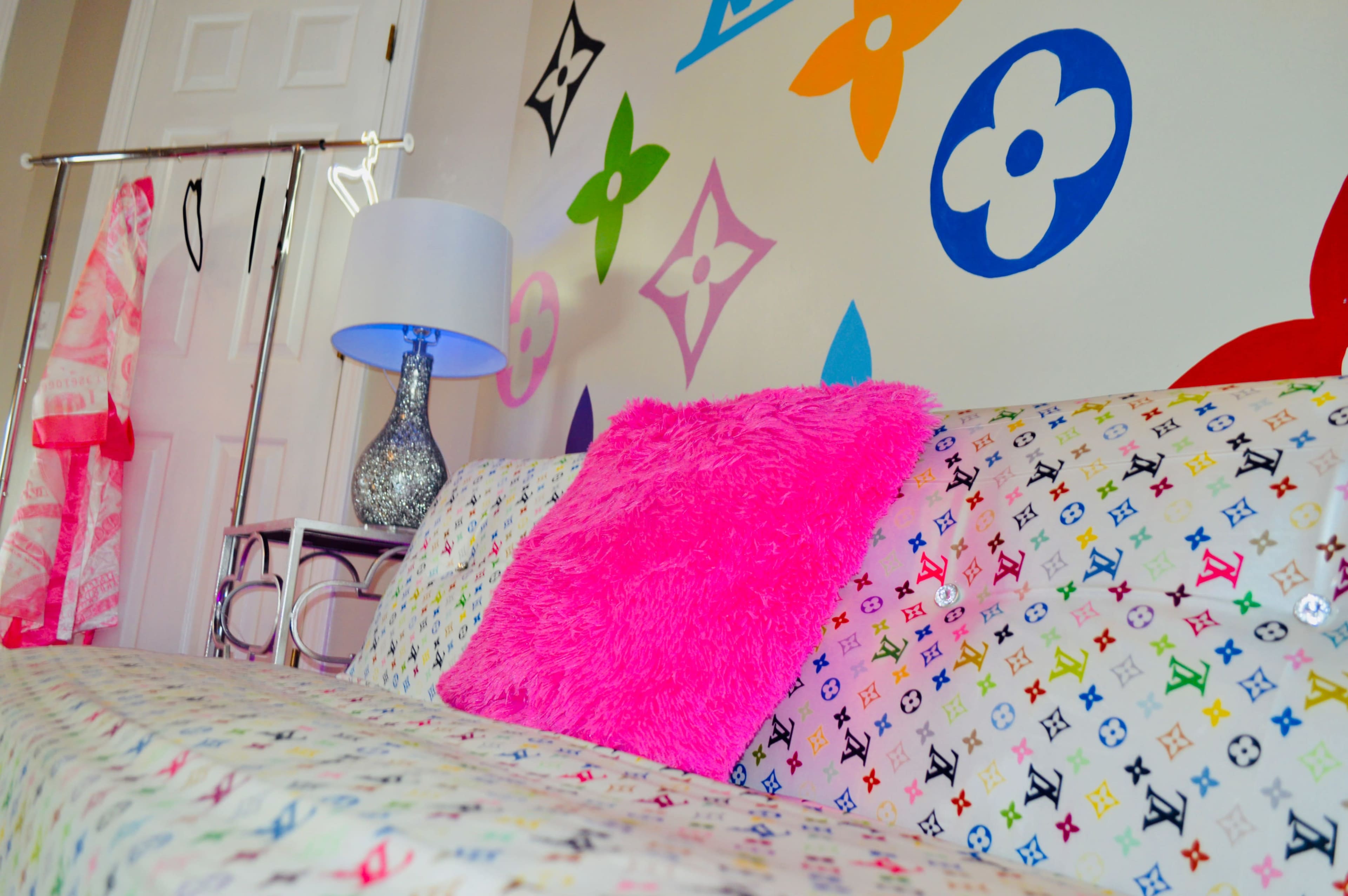 The image shows a colorful couch adorned with a bright pink pillow, set against a wall decorated with various flower and logo designs.