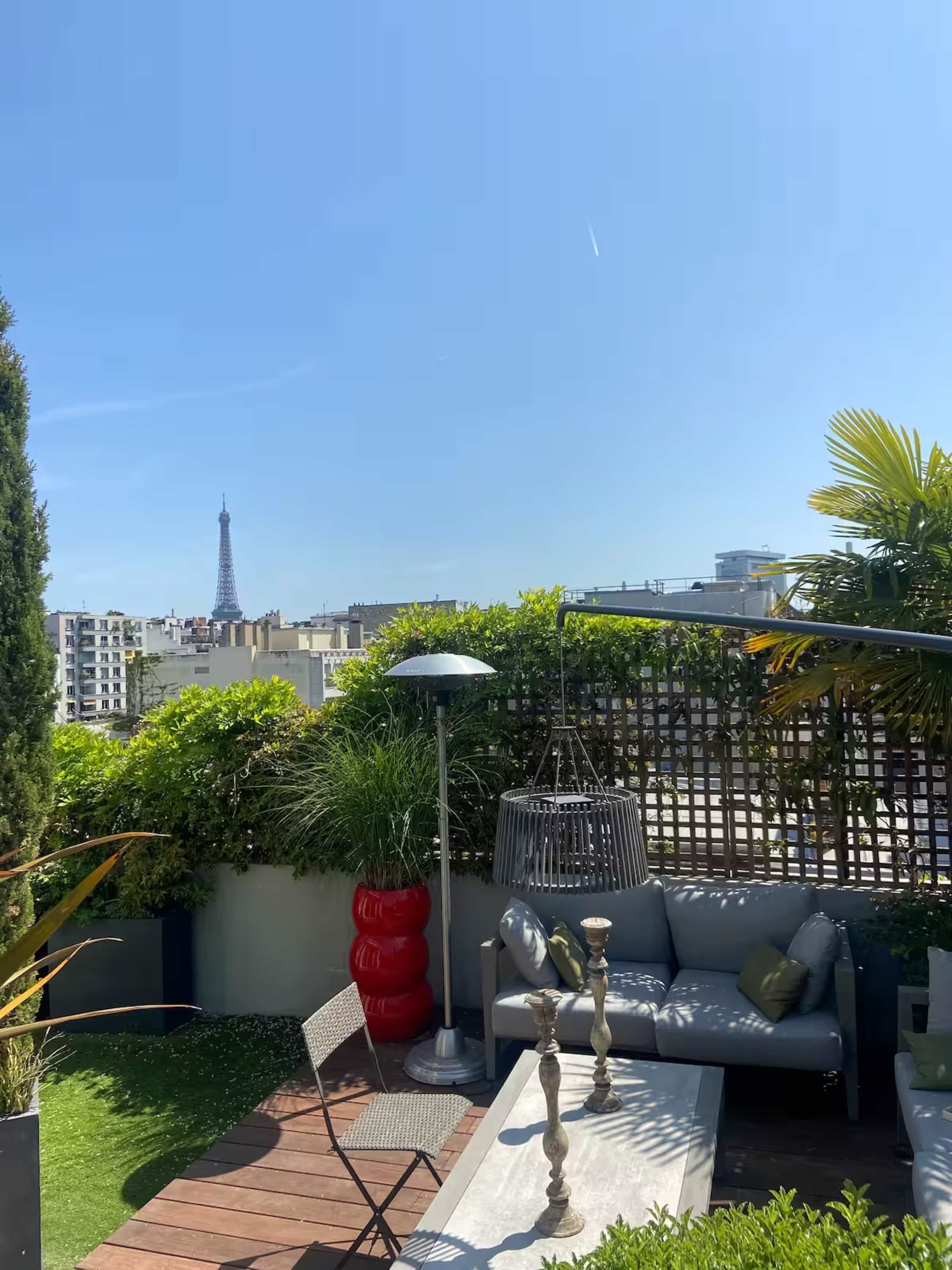 The image shows a rooftop terrace with a seating area, a decorative birdcage, and the Eiffel Tower visible in the background against a clear blue sky.