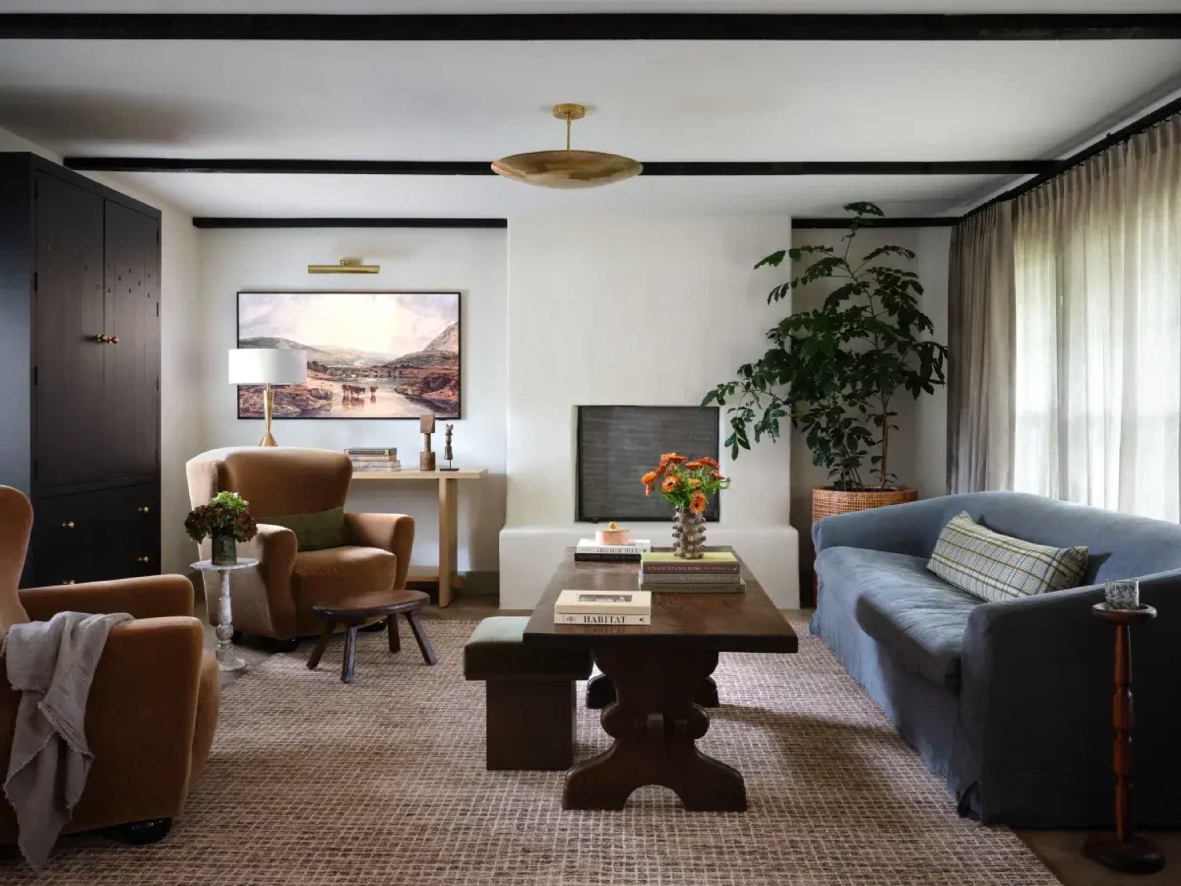 The living room features a mix of seating arrangements, including a blue sofa and two brown armchairs, with a coffee table at the center and a large plant in the corner.