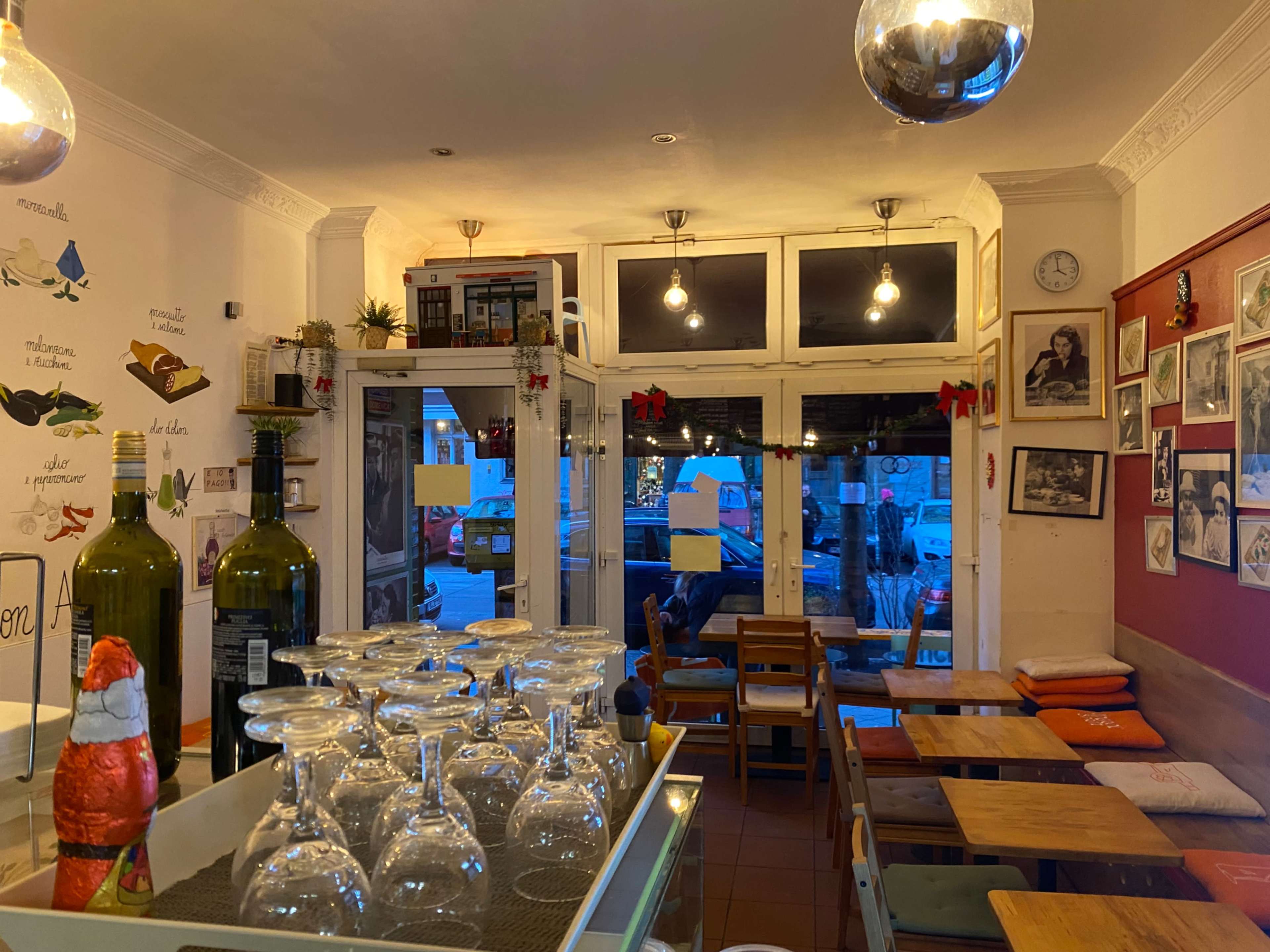 The image shows the interior of a cozy restaurant with wooden tables, glassware stacked upside down, and decorative wall art, illuminated by warm lighting.