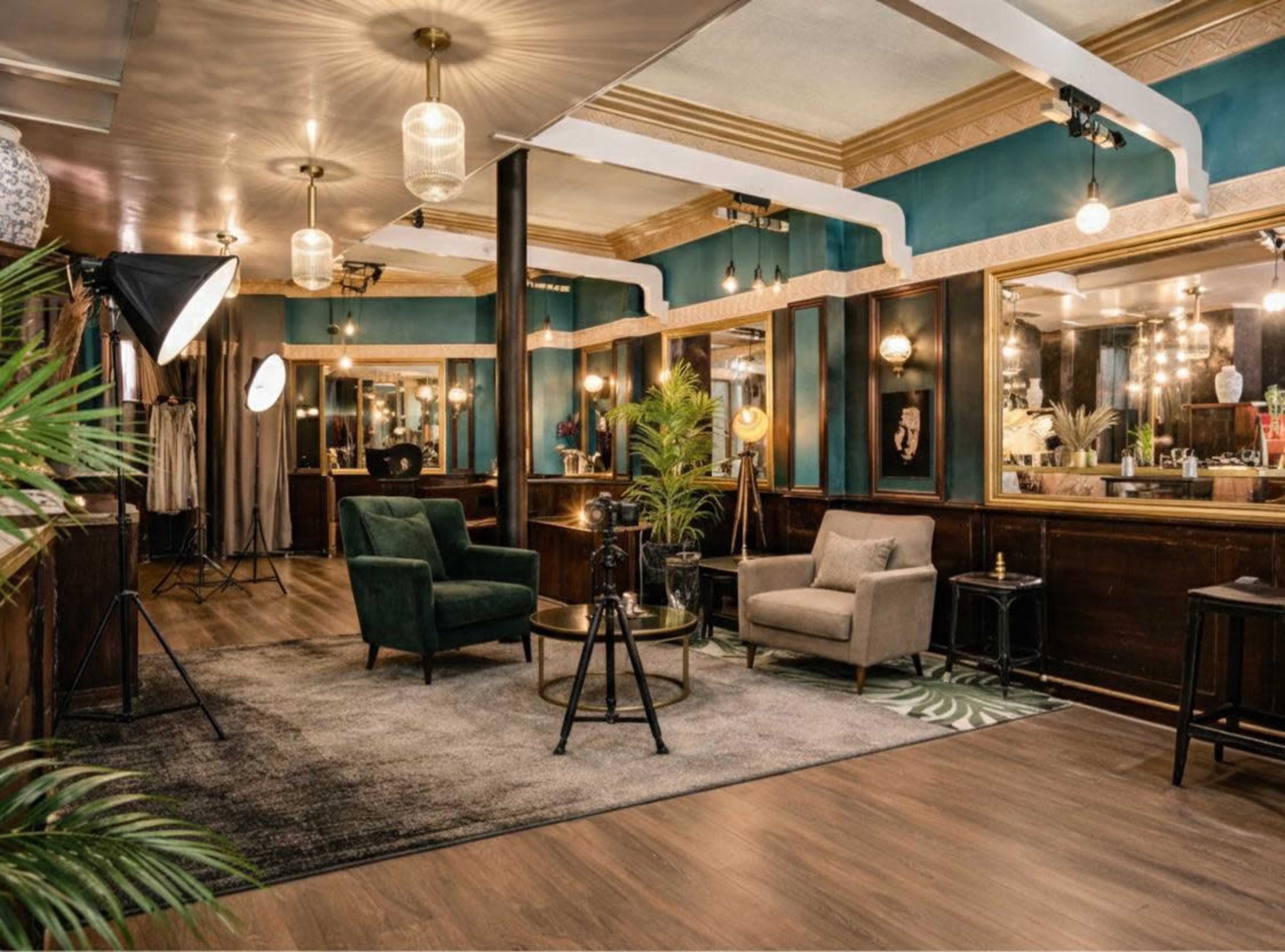 The image shows an elegantly designed interior of a salon featuring two armchairs, a coffee table, and large mirrors, with warm lighting and decorative plants.