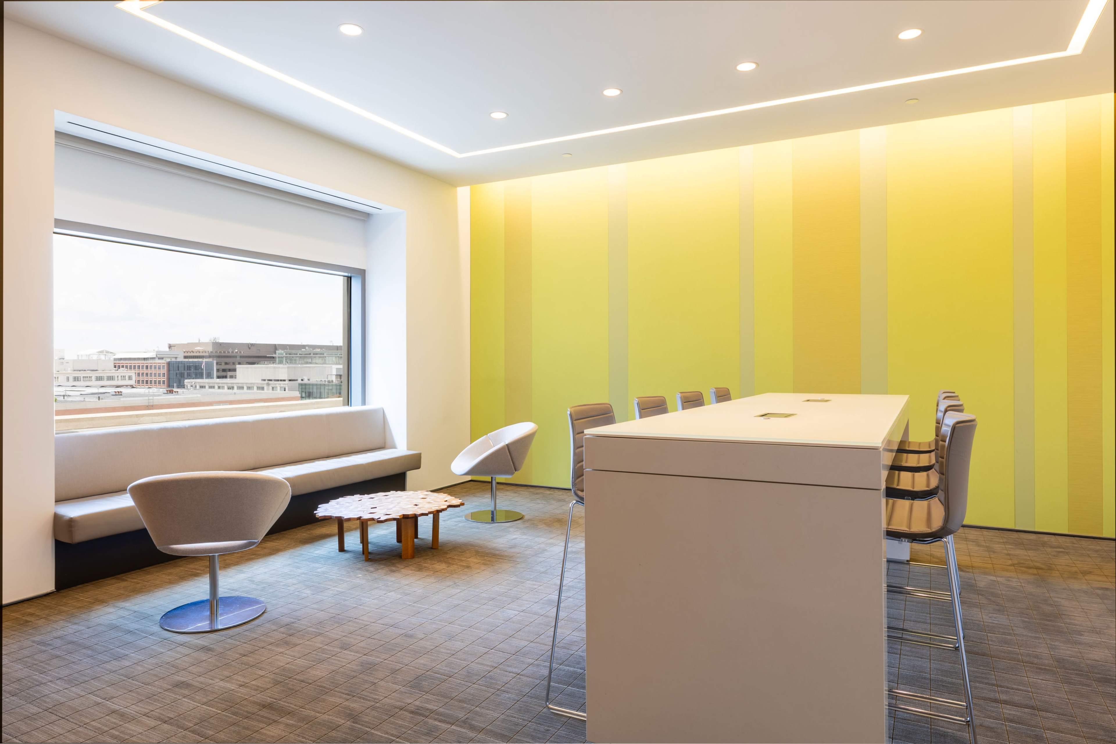 The image depicts a modern conference room with a long white table, several chairs, and a large window providing a view of the outside.