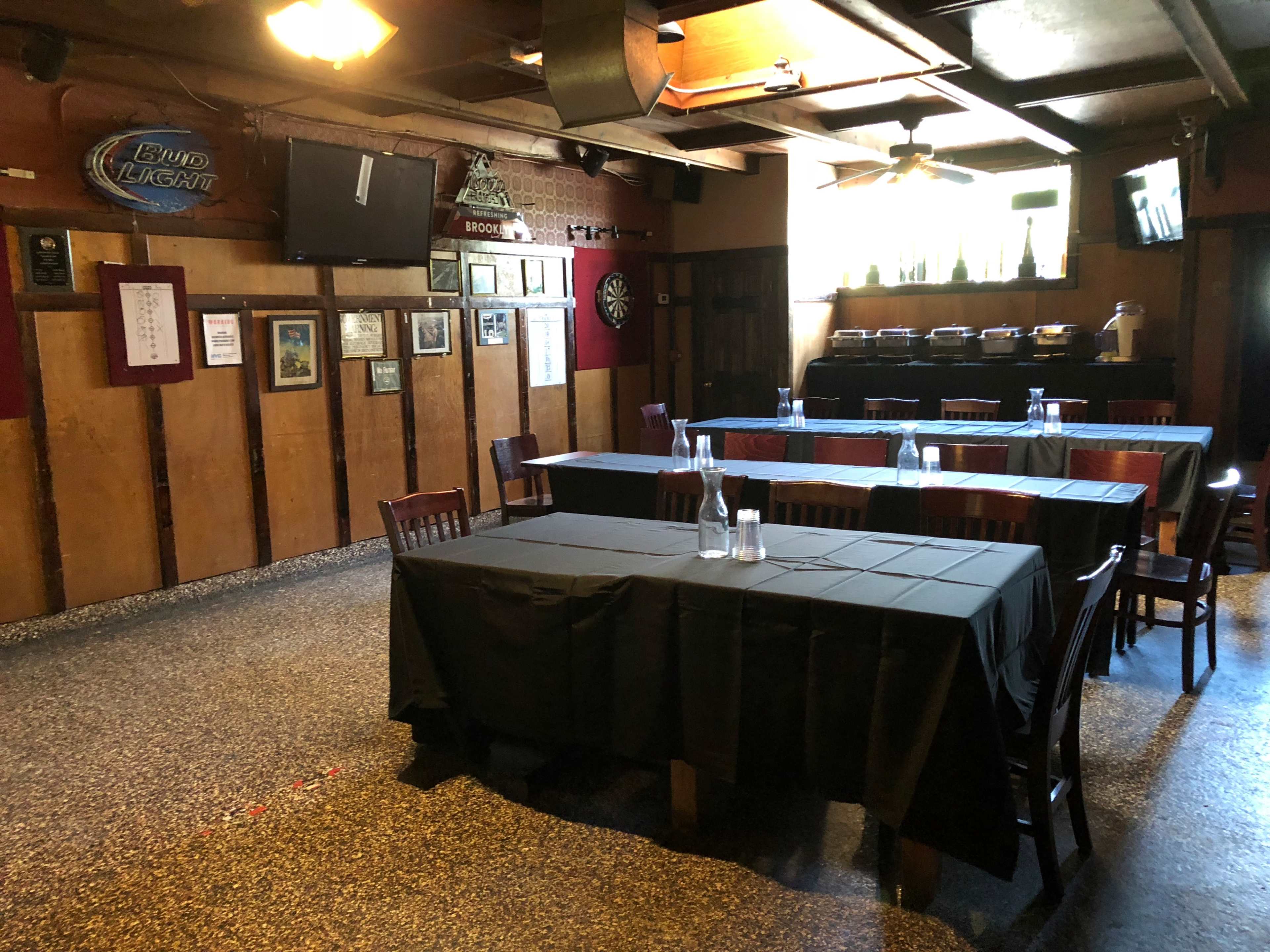 An empty dining area in a bar or pub, featuring several tables covered with black tablecloths and a small stage or platform in the background.