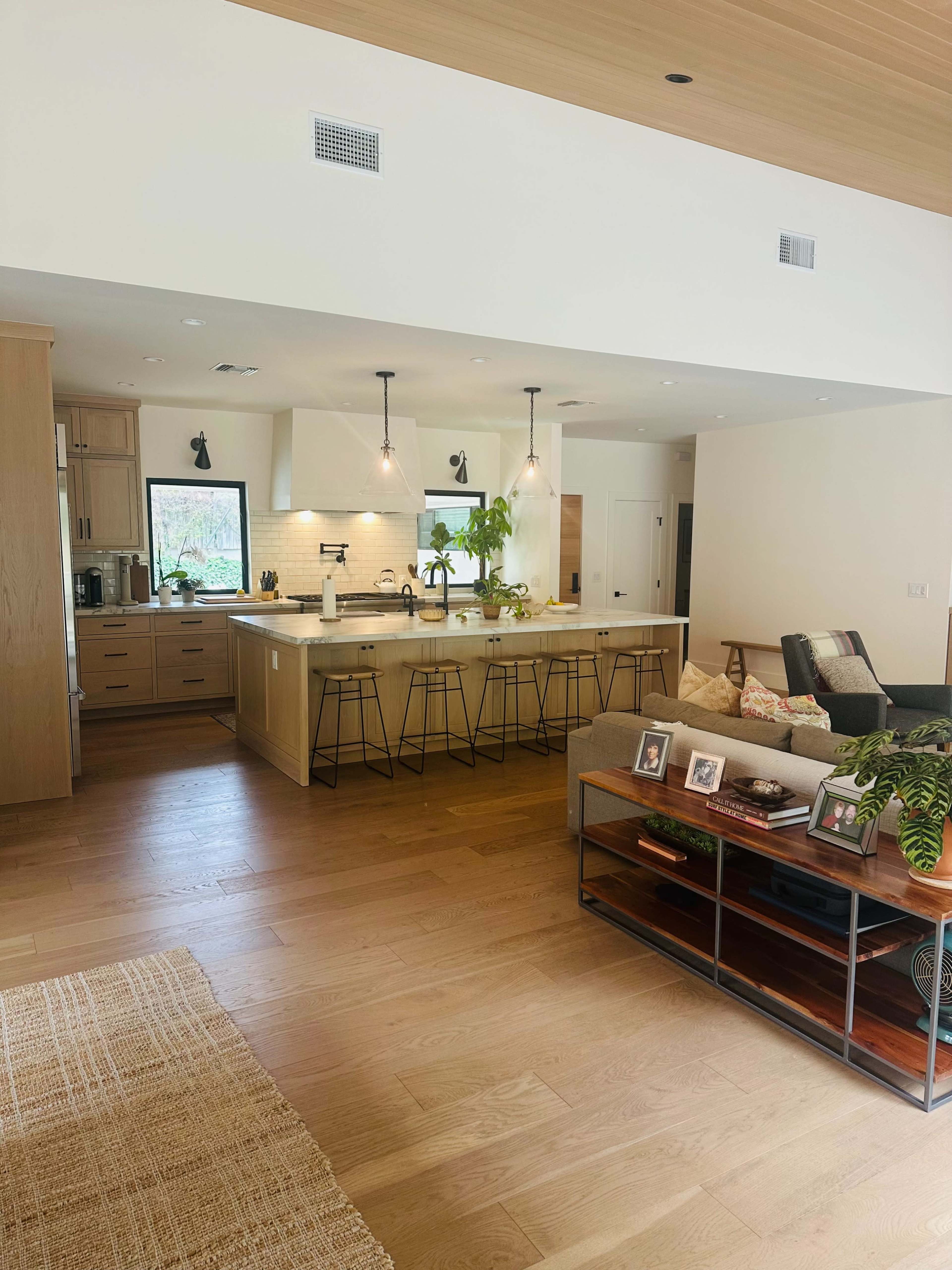 A bright, modern living space features a kitchen island with bar stools, a cozy seating area with a sofa, and natural wood accents throughout.