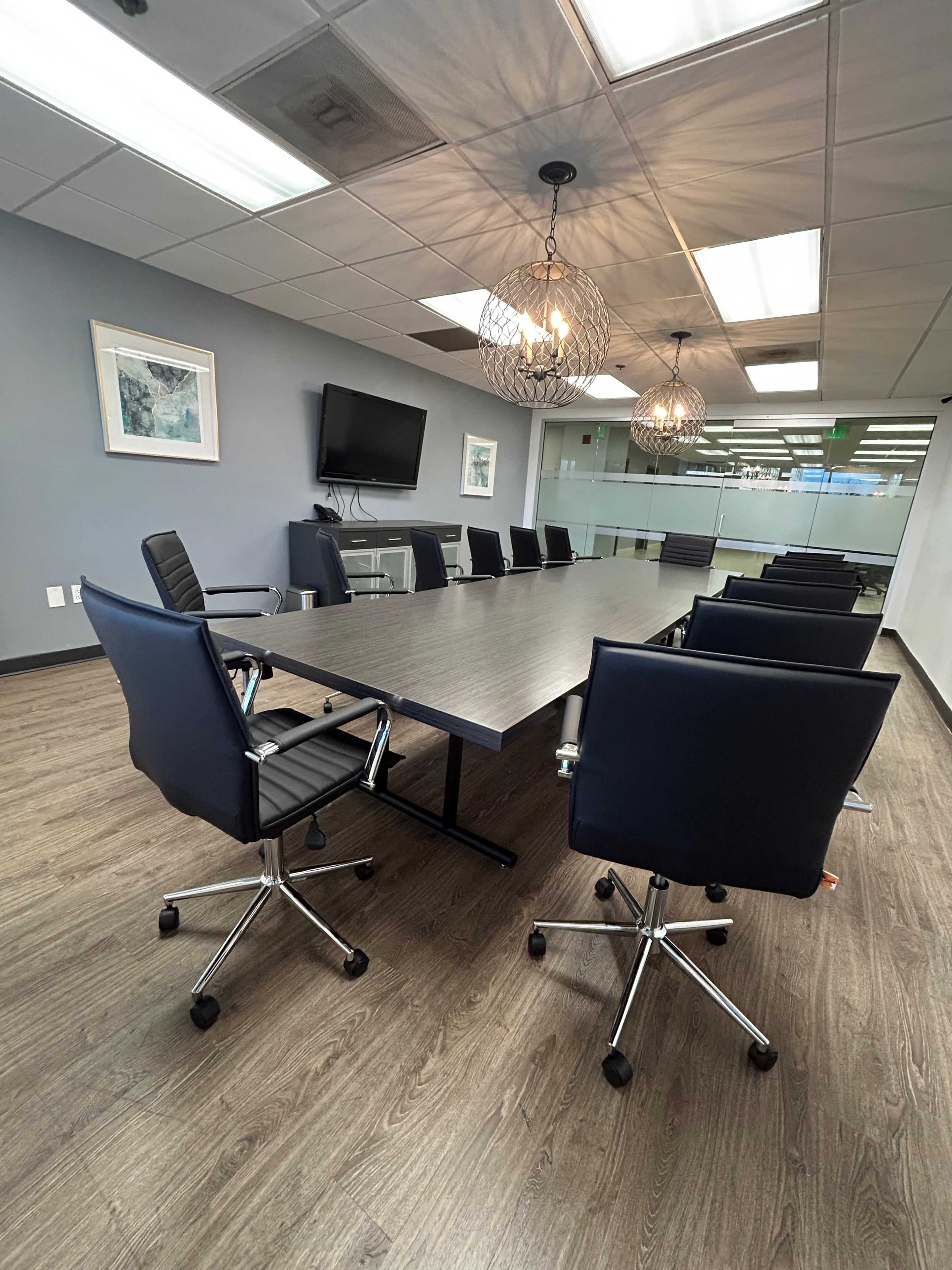 The image shows a modern conference room featuring a large rectangular table surrounded by ergonomic chairs and two pendant lights overhead.