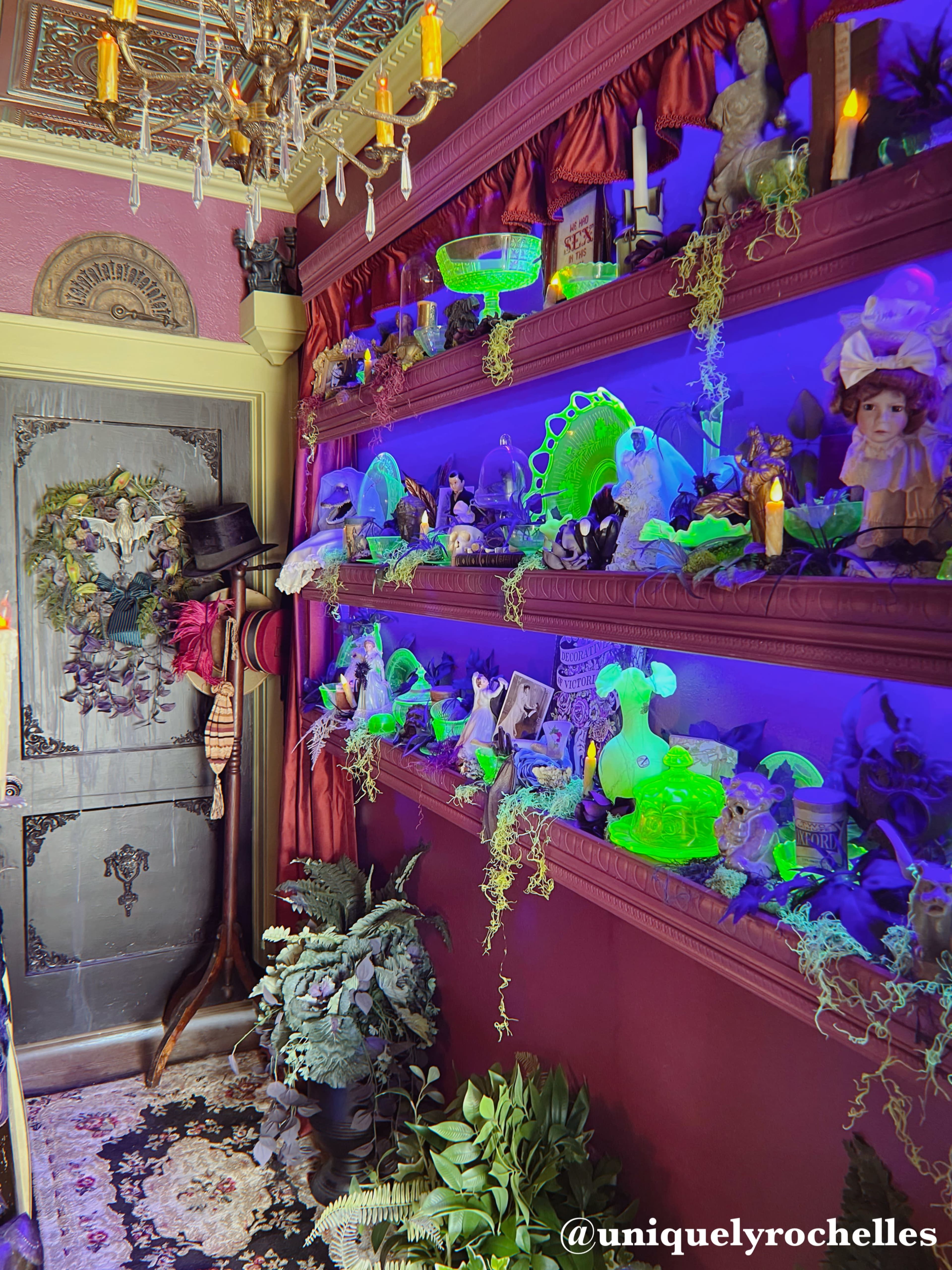 The image shows a vividly decorated interior wall with shelves displaying various objects, including illuminated figurines and plants, under purple lighting.
