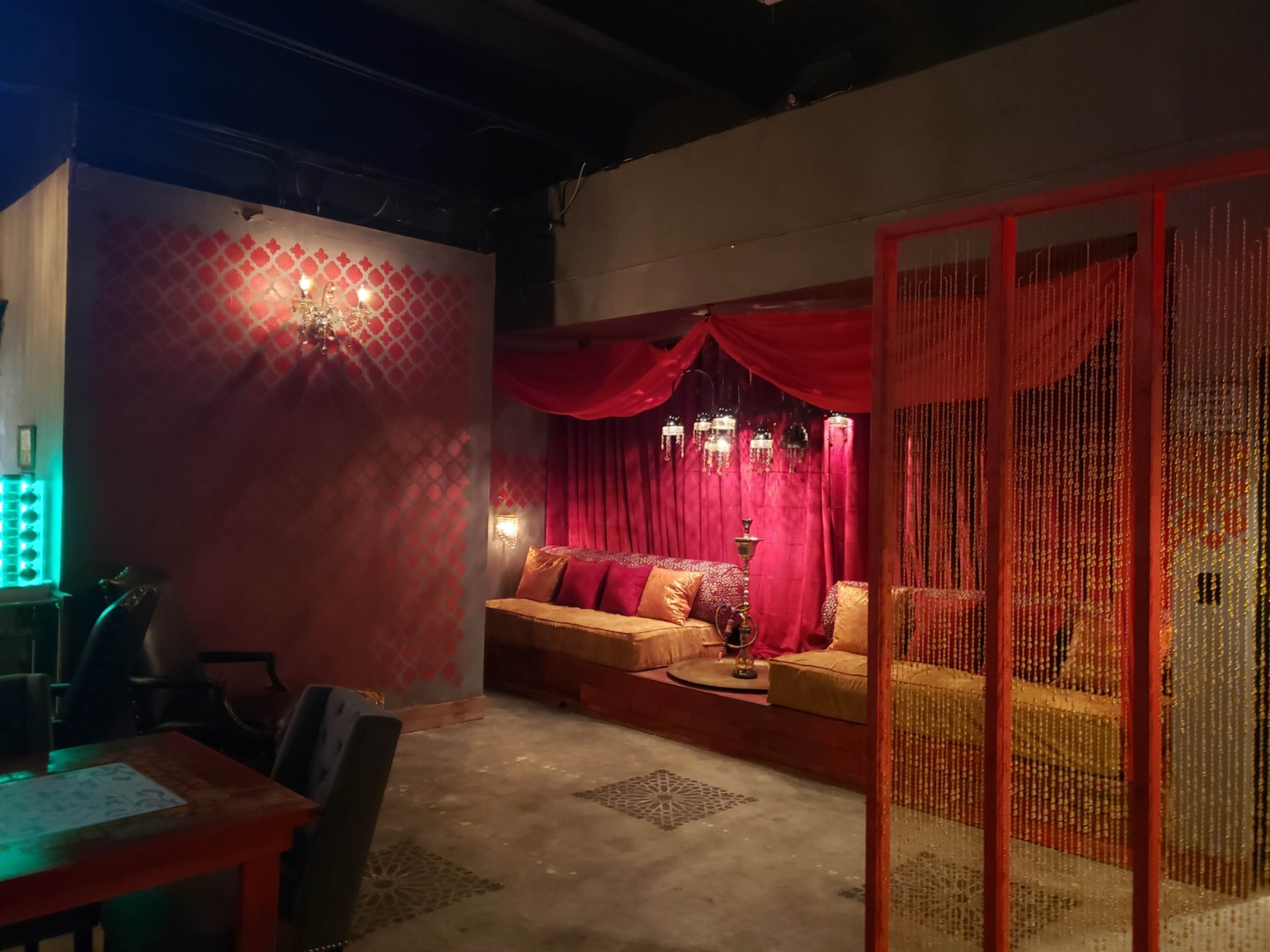 The image shows a dimly lit lounge area with purple drapes, comfortable seating, and decorative lighting.