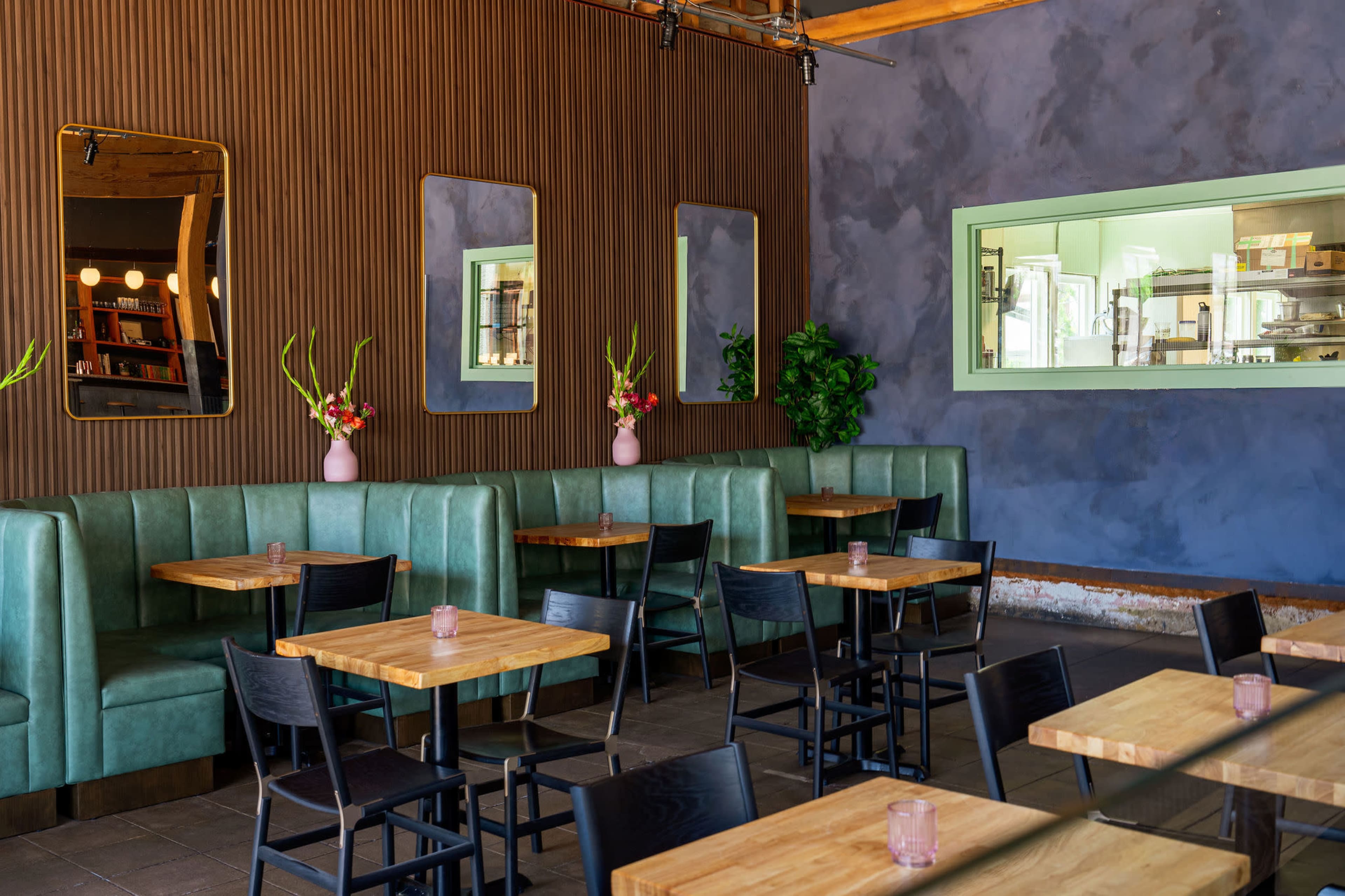 A modern restaurant interior featuring green booths along the walls, wooden tables, and large mirrors.