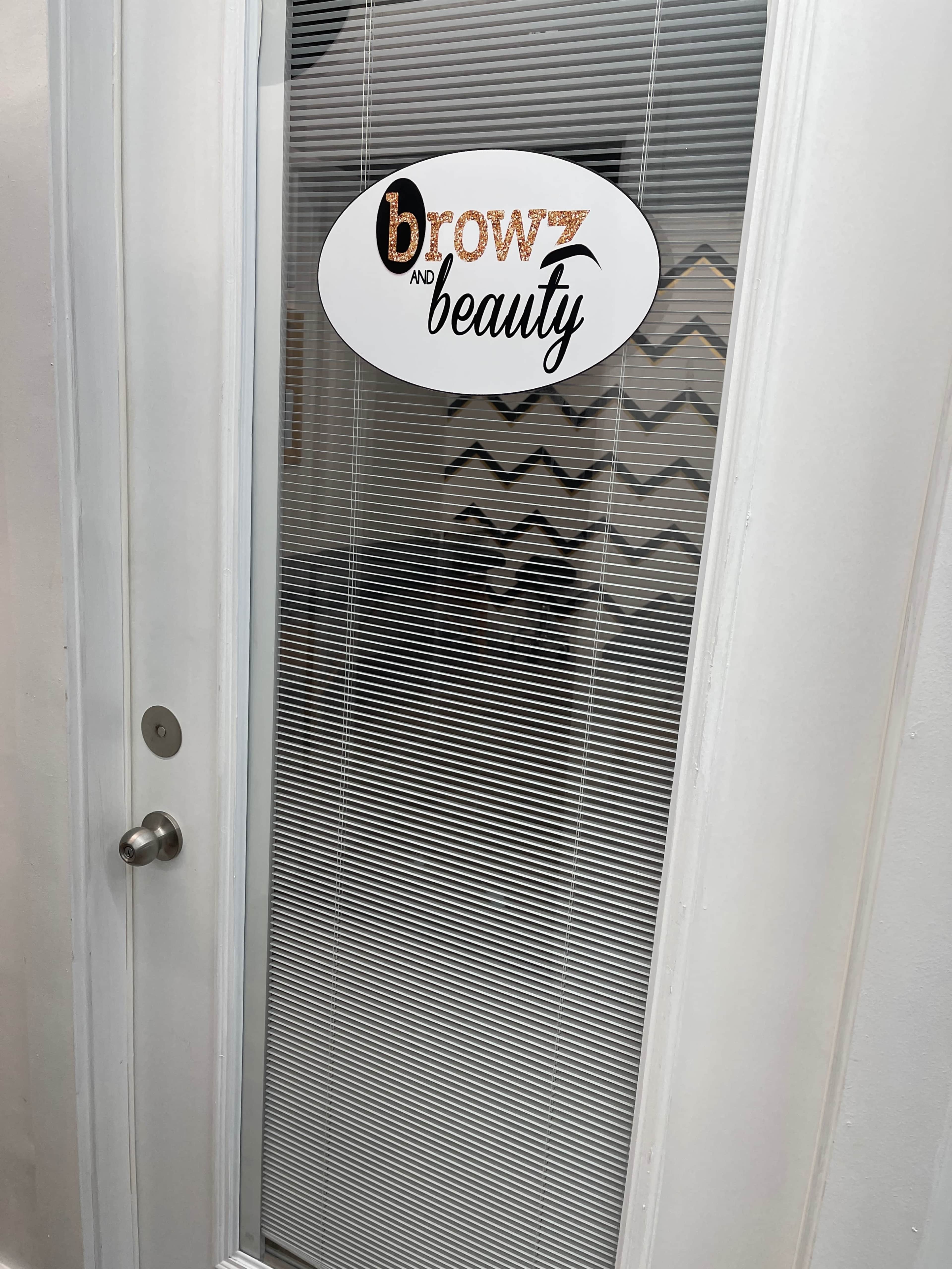 A door with a sign that reads "browz and beauty" on a glass panel featuring horizontal lines.