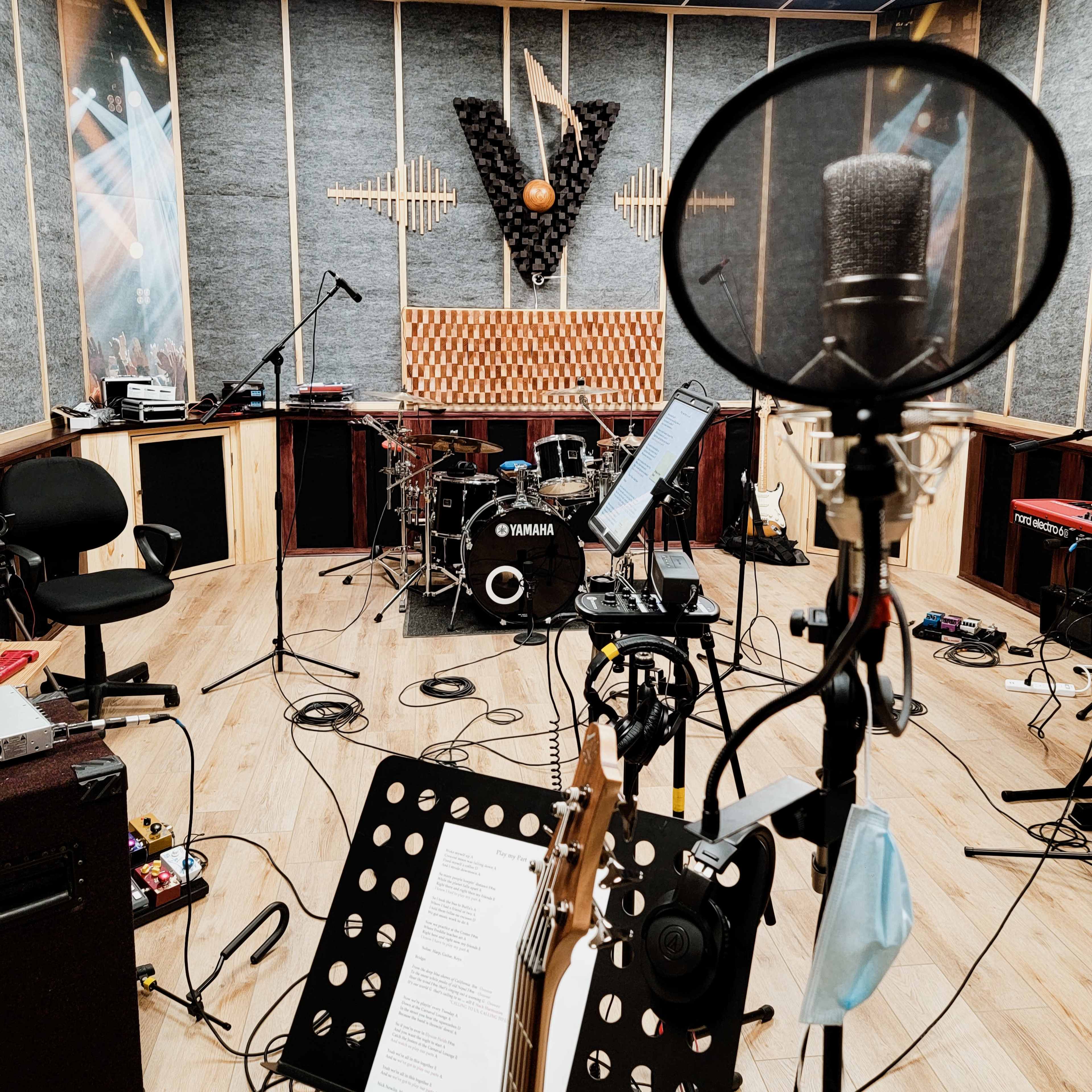 A recording studio is equipped with various instruments, including a drum set, microphones, and a guitar, arranged for a music session.