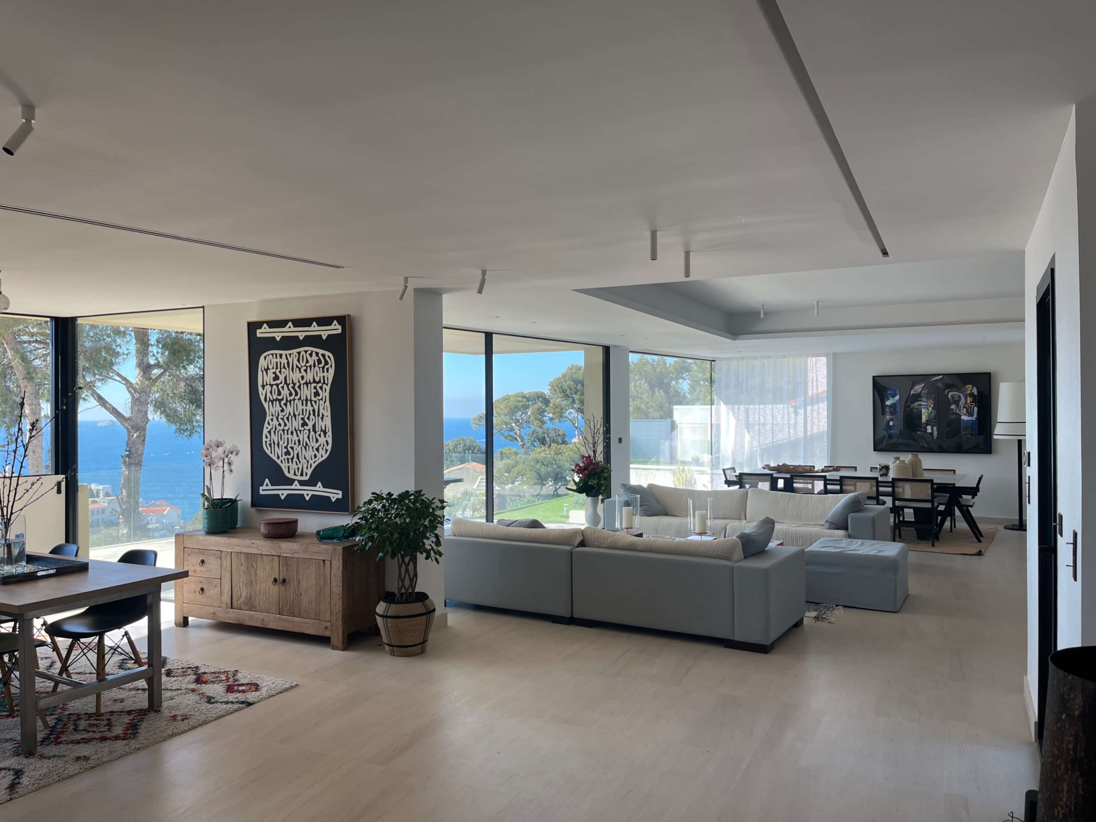 A modern open-concept living space features large windows that provide a view of the ocean and is furnished with a dining area, seating arrangements, and decorative elements.