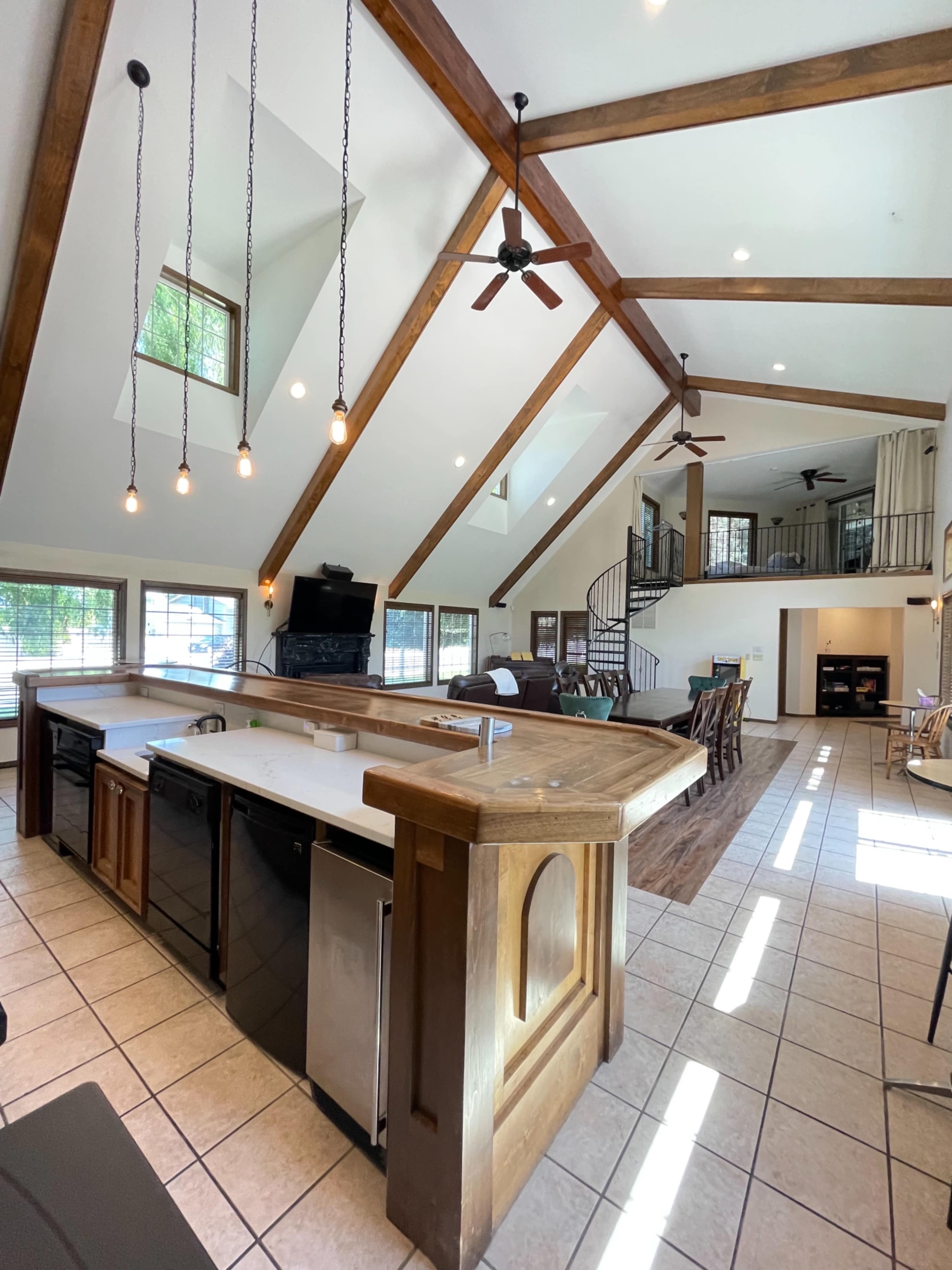 A spacious kitchen with a large island, featuring modern appliances, high wooden beams overhead, and ample natural light entering through large windows.