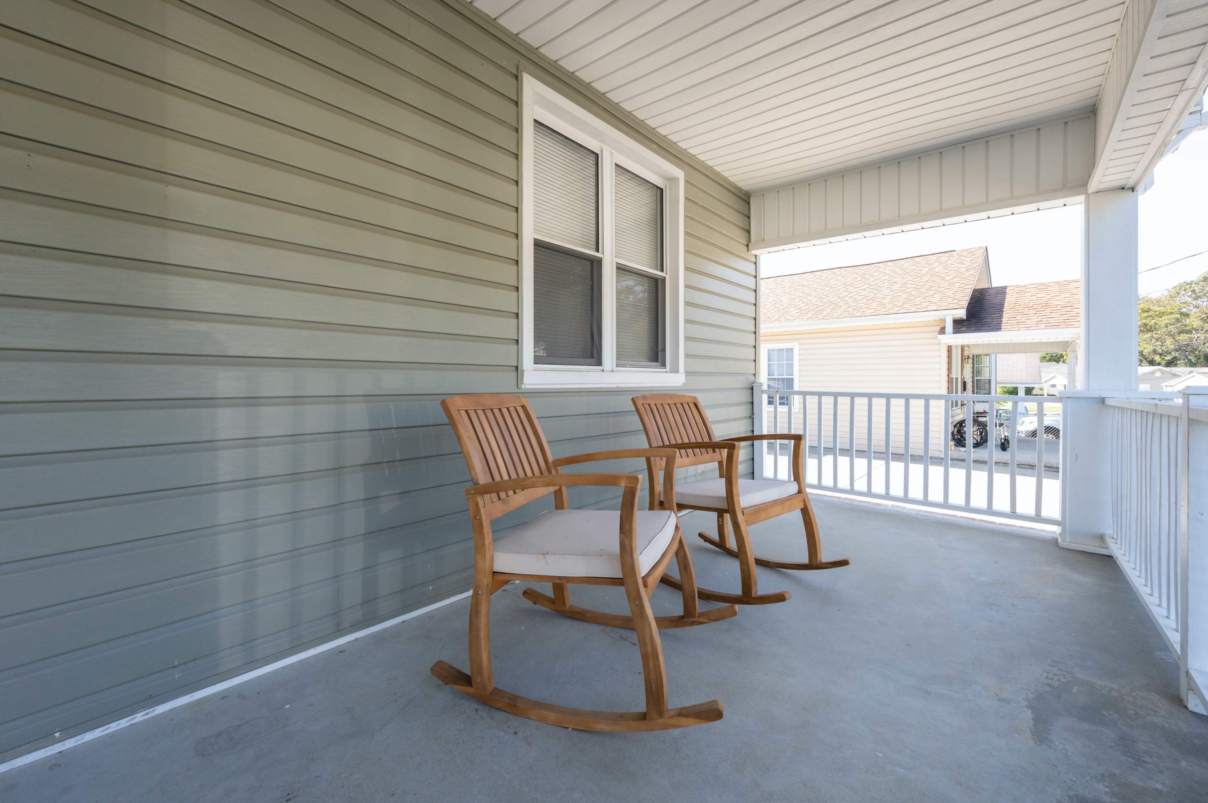 A porch with two wooden rocking chairs positioned side by side against a light green wall.