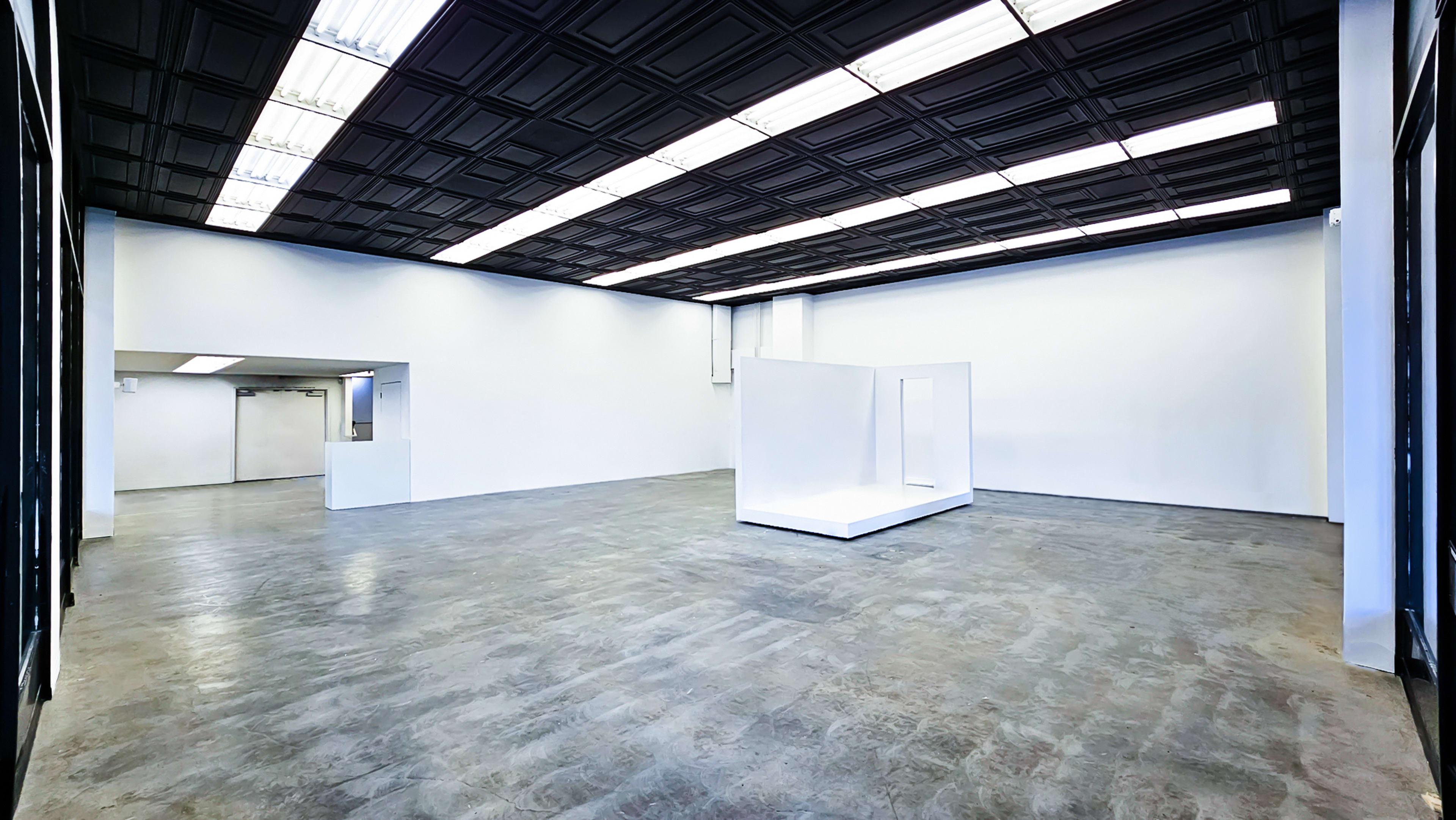 A spacious, minimalist art gallery features white walls, a clear floor, and a central white display structure.