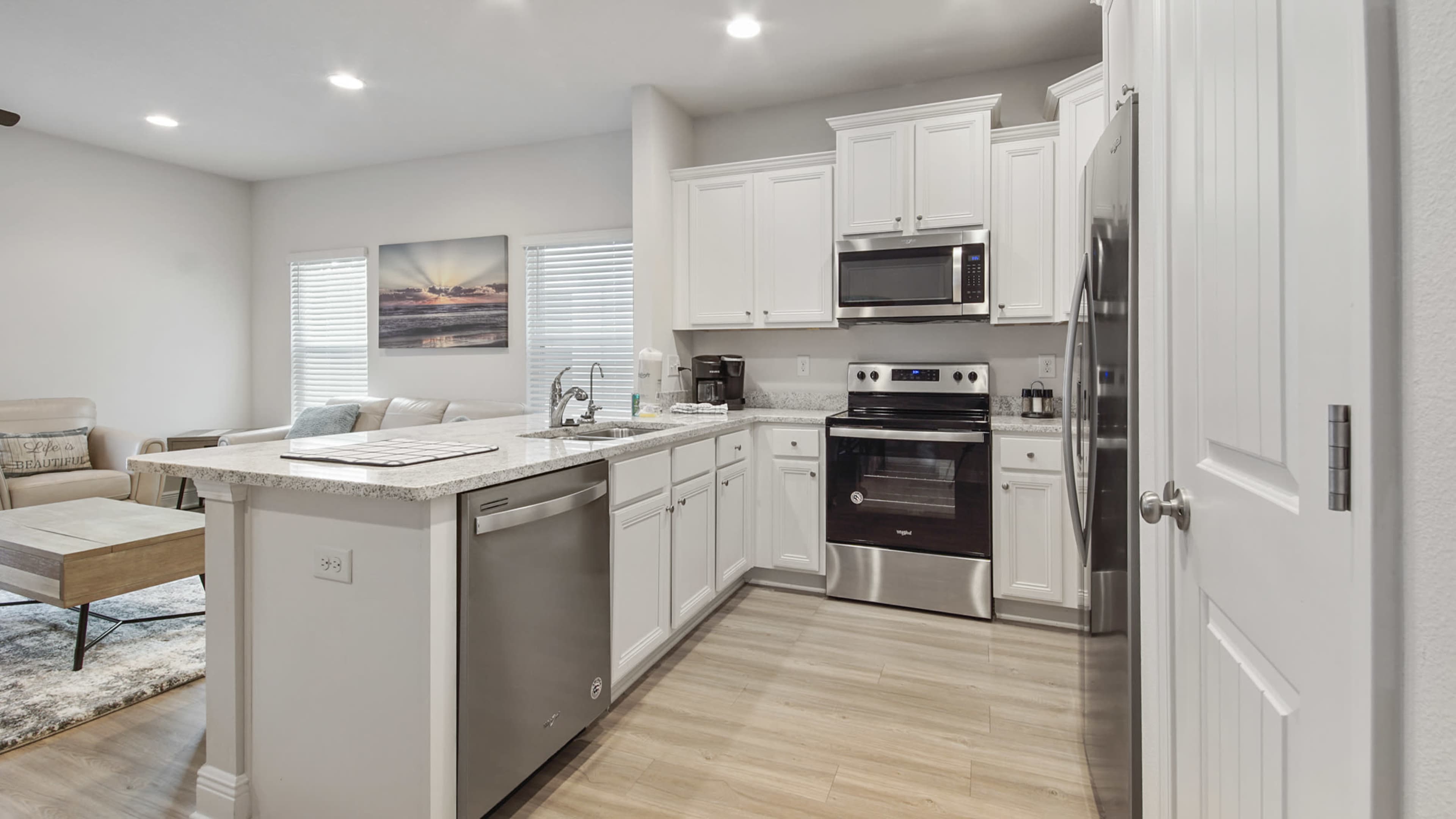 A modern kitchen features white cabinetry, stainless steel appliances, and a view into a living area with a light-colored sofa.