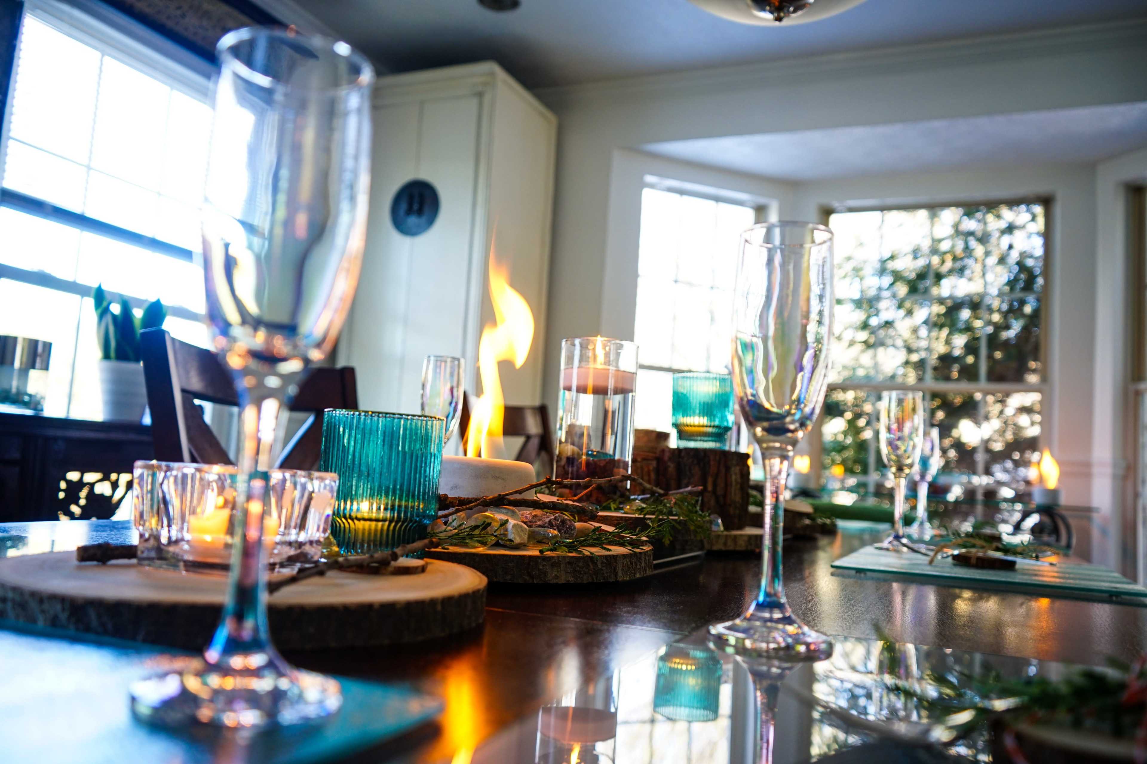 A dining table set with glassware and candles, featuring a centerpiece with flames and decorative elements.
