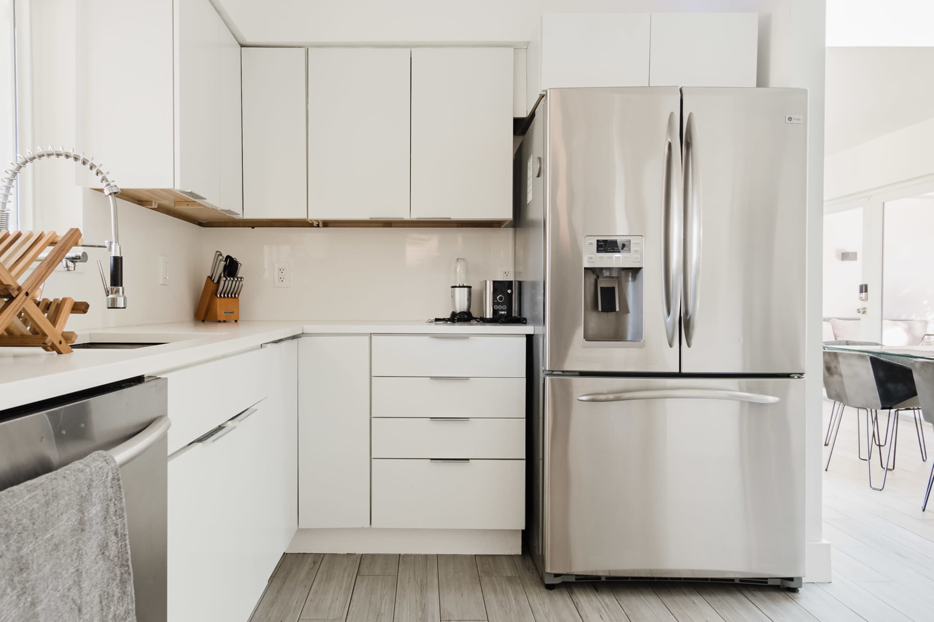 A modern kitchen with white cabinetry, a stainless steel refrigerator, a sink, and a wooden countertop.