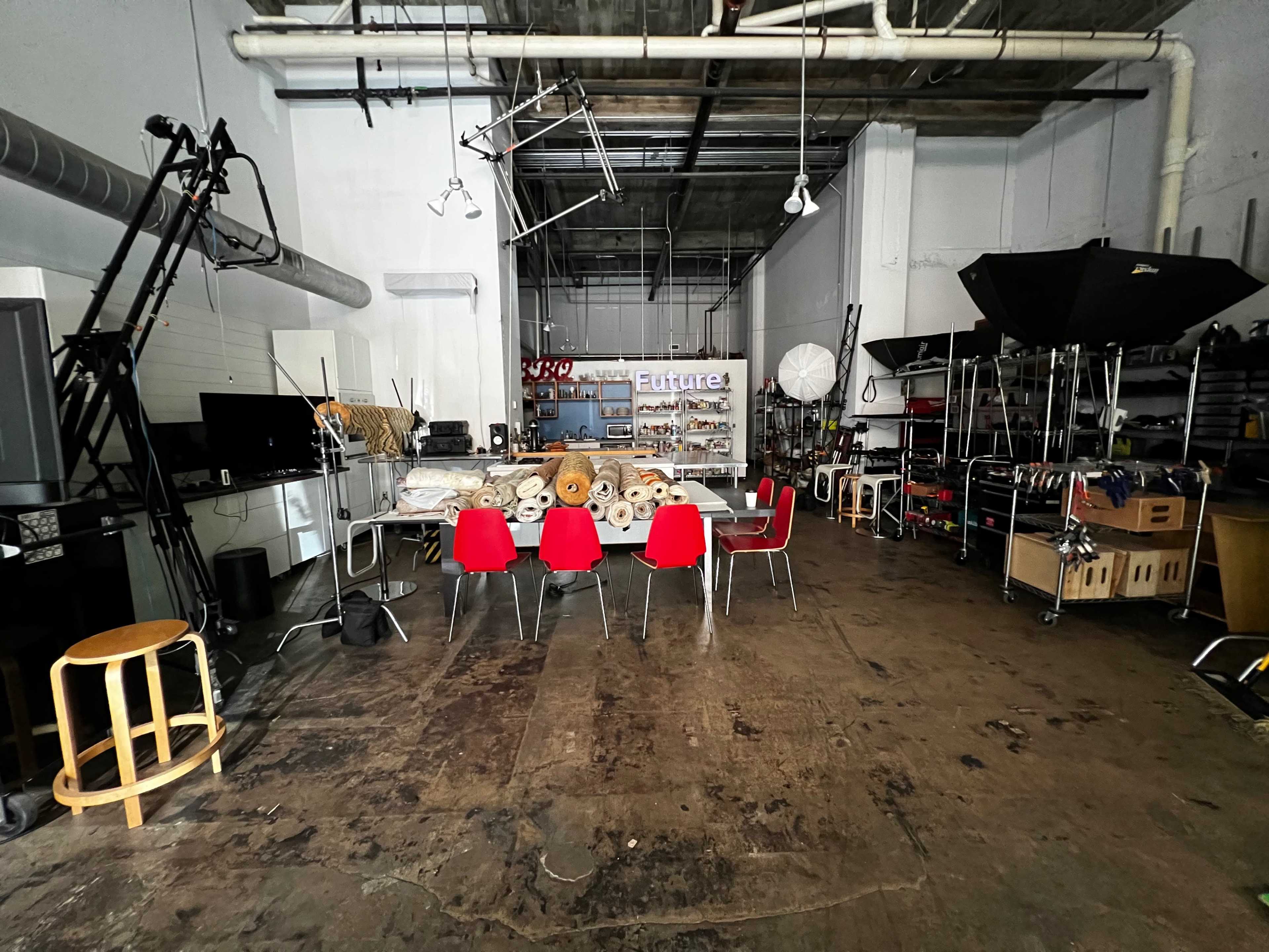 The image shows a spacious studio with red chairs arranged around a table, surrounded by various equipment and storage shelves.