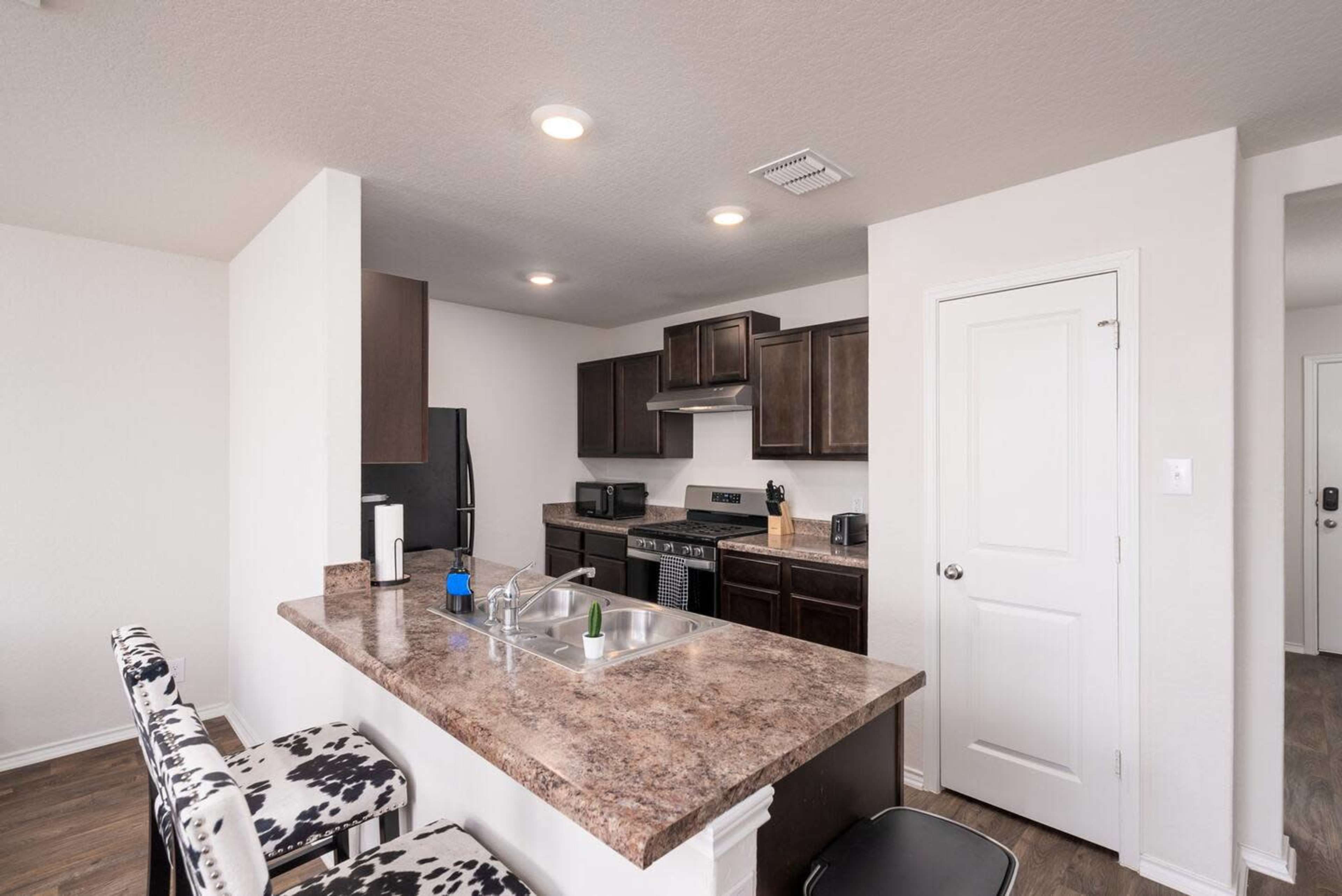 A modern kitchen with dark cabinetry, a stainless steel stove, and bar seating with patterned stools.