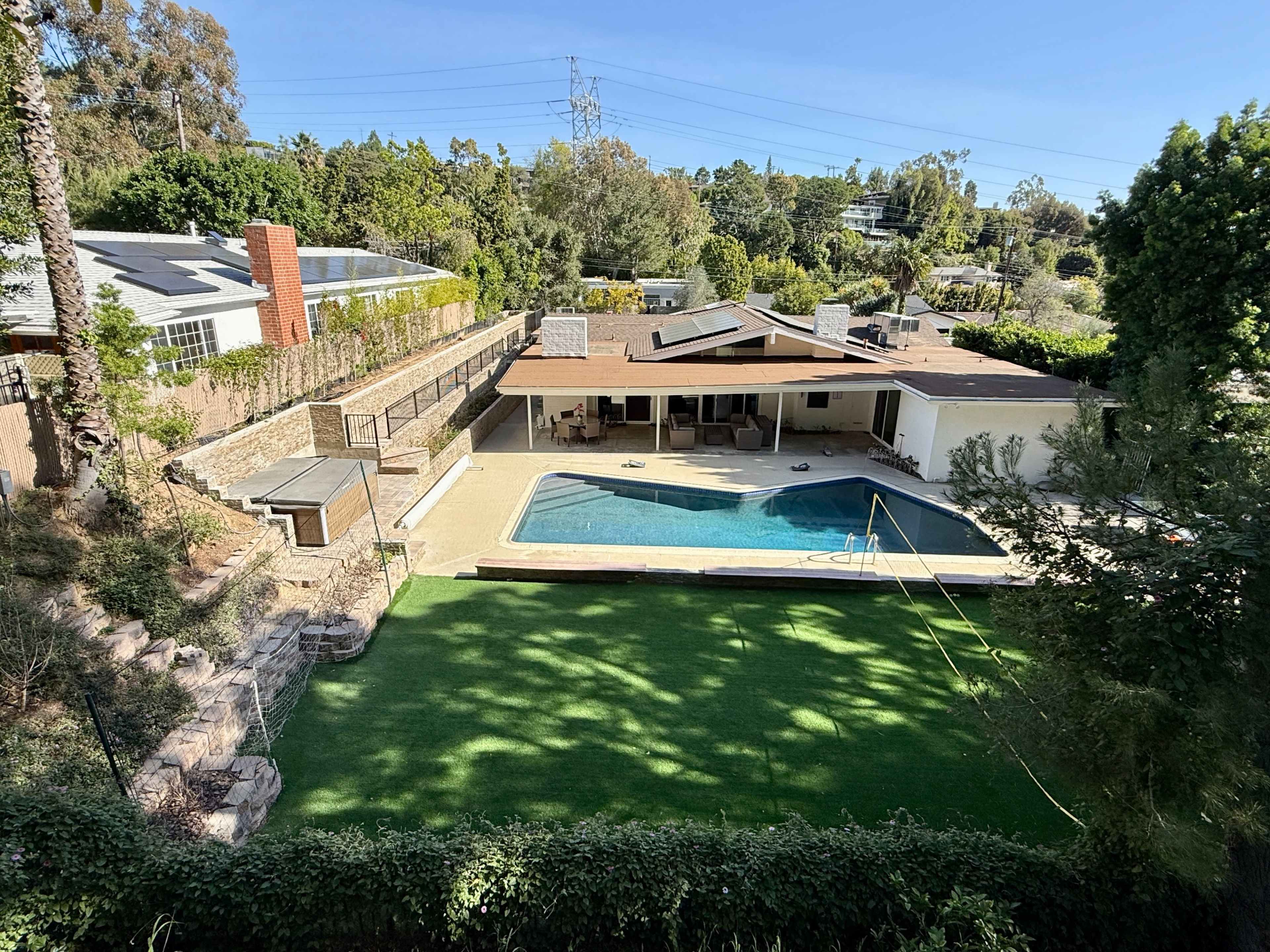 The image shows a modern house with a swimming pool and a grassy yard surrounded by trees and landscaping.