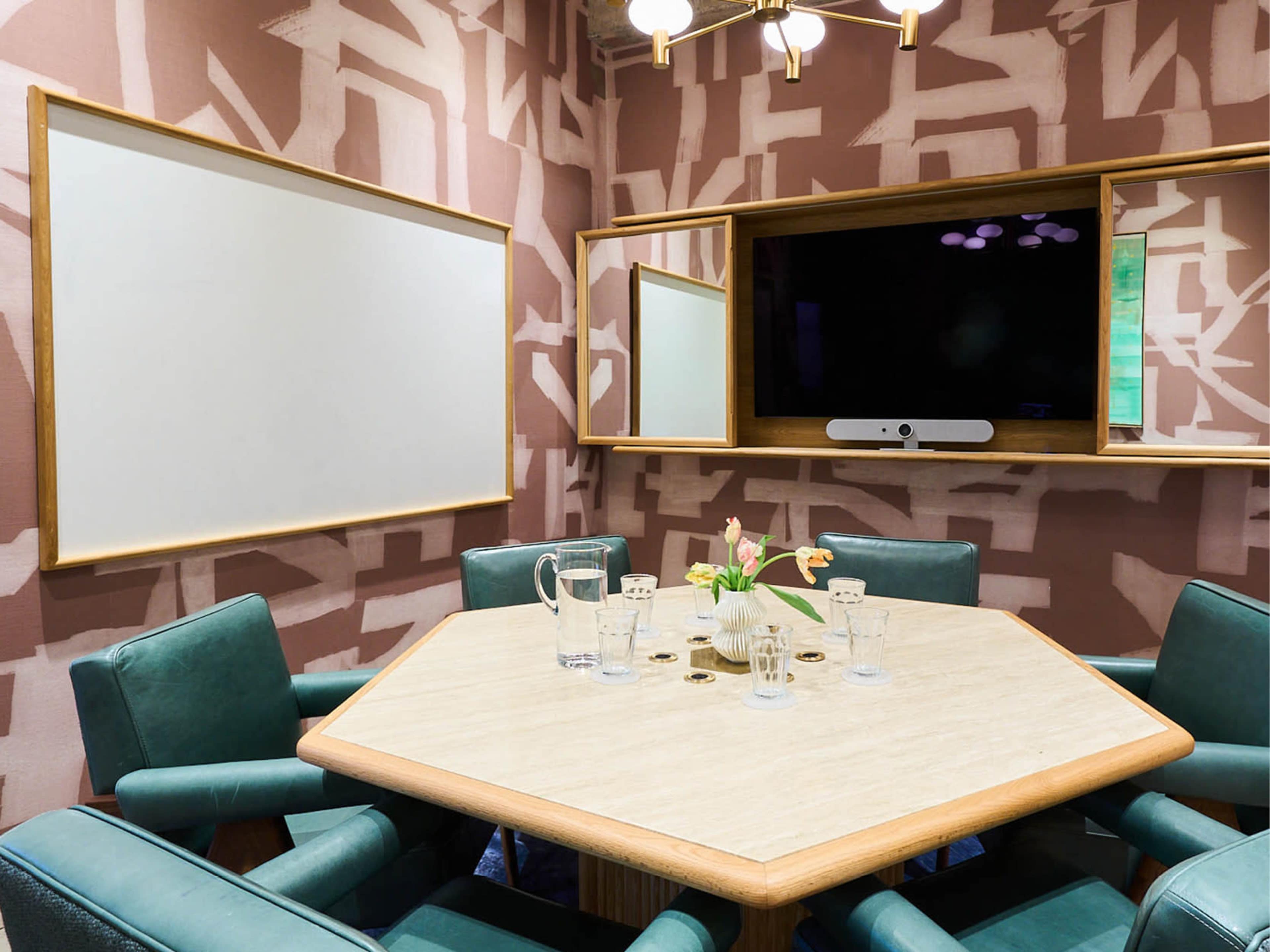 The image shows a conference room with an octagonal table surrounded by green chairs, a television, and two blank whiteboards against a patterned wall.