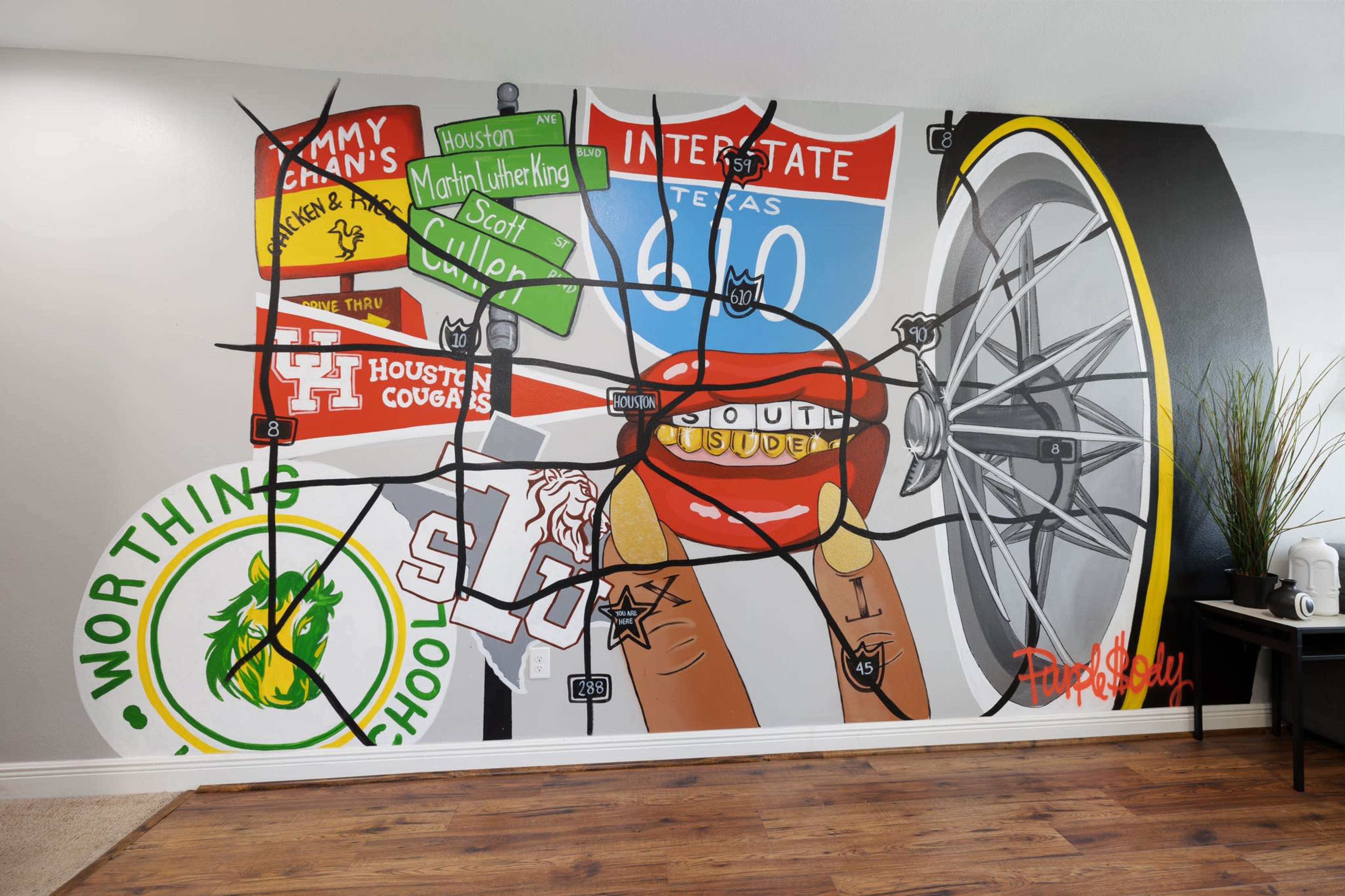 A colorful mural featuring various elements such as a bicycle wheel, school logos, and street signs on a wall.