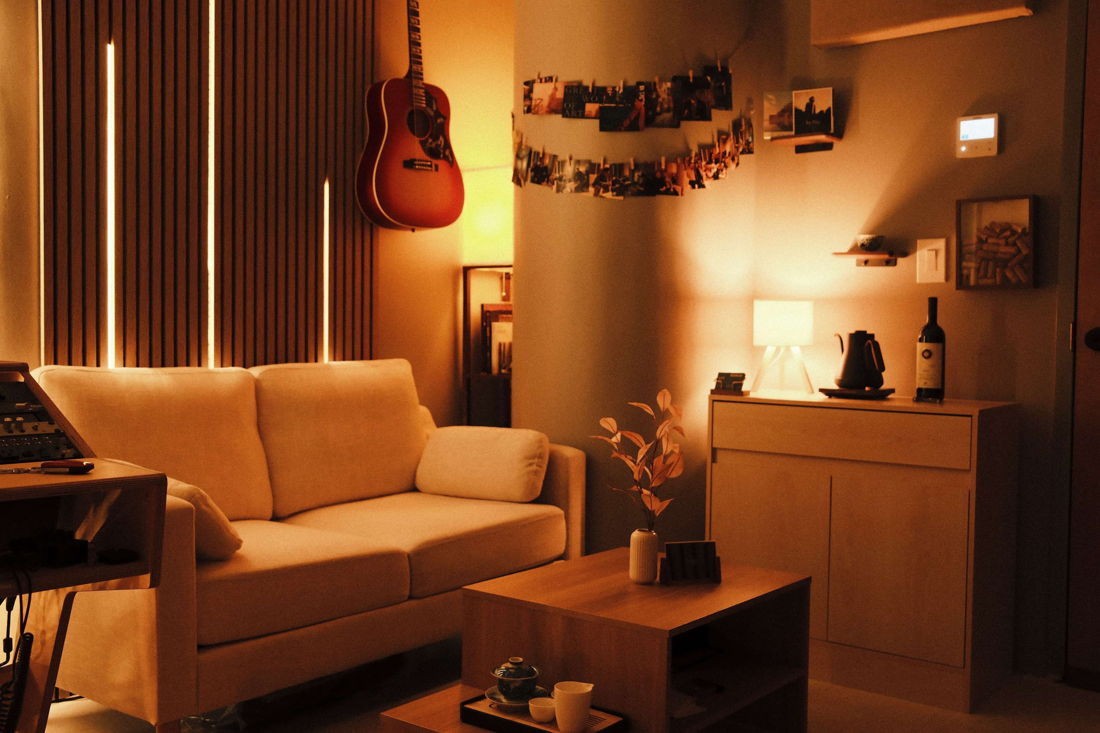 A cozy living room features a white sofa, a coffee table, and an acoustic guitar hanging on the wall, illuminated by warm lighting.