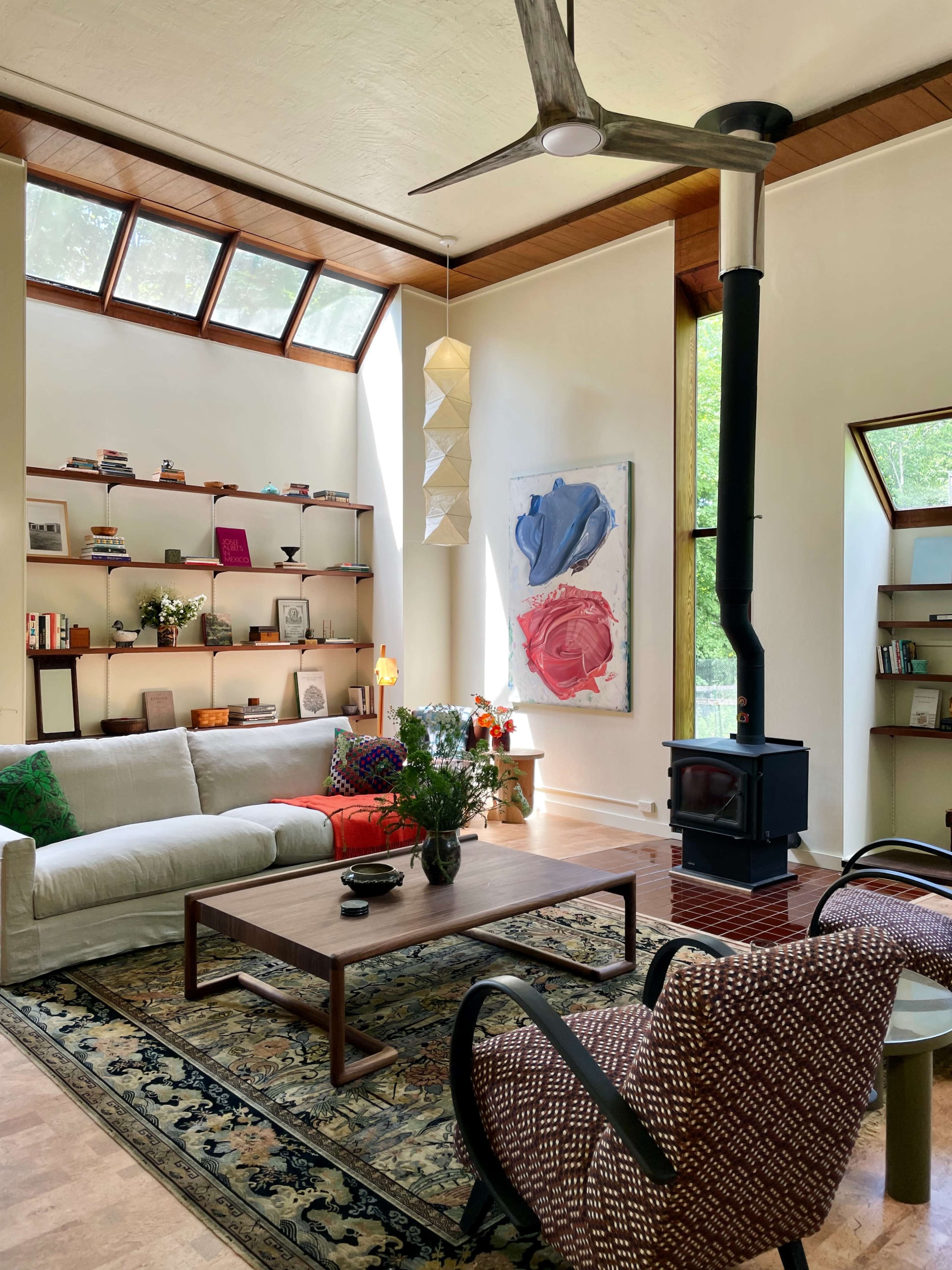 A bright, modern living room features a white sofa, a wooden coffee table, and a wood-burning stove, with shelves filled with books and decorative items.