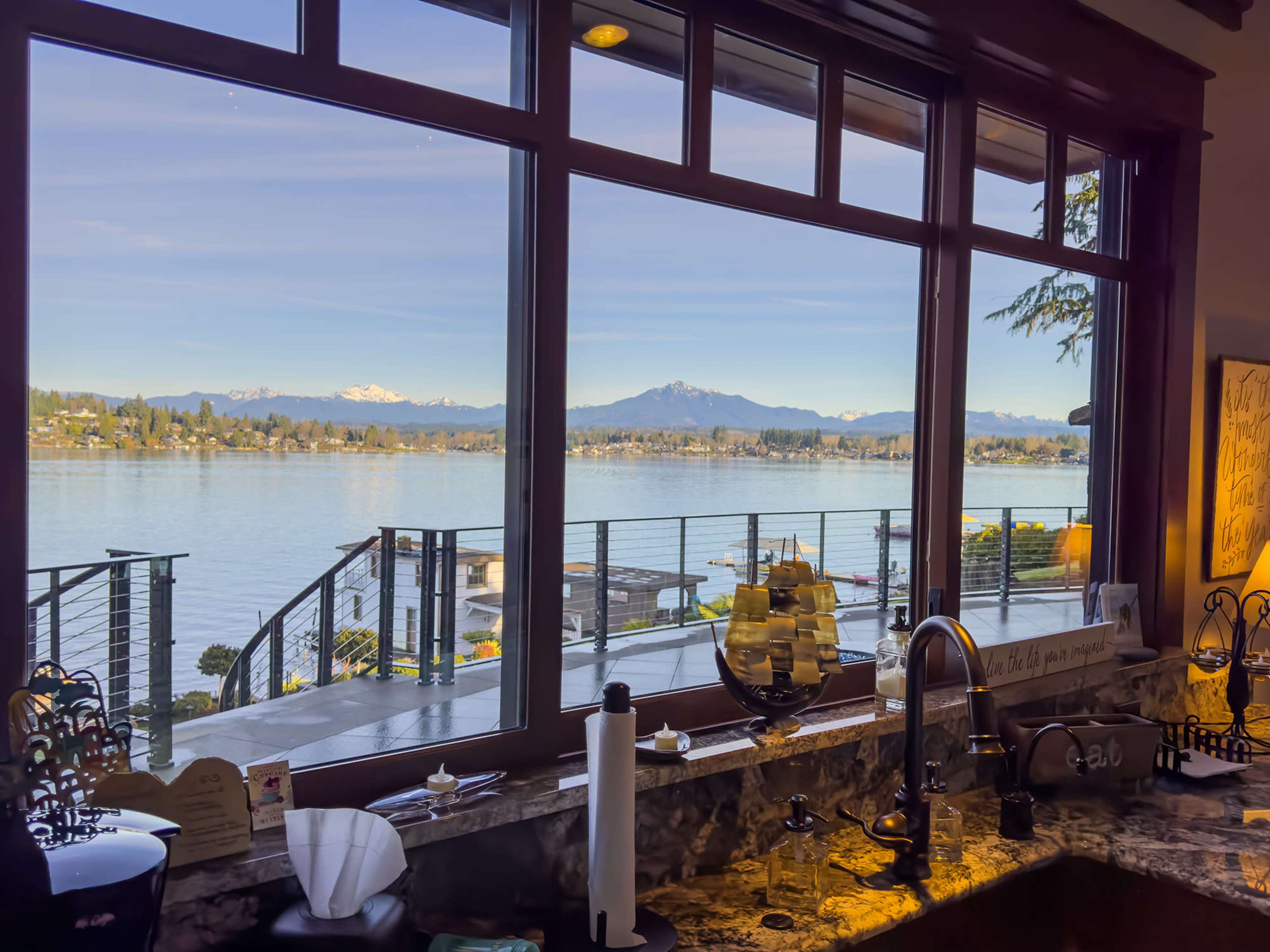 A panoramic view of a lake and mountains is framed by large windows in a well-furnished interior.