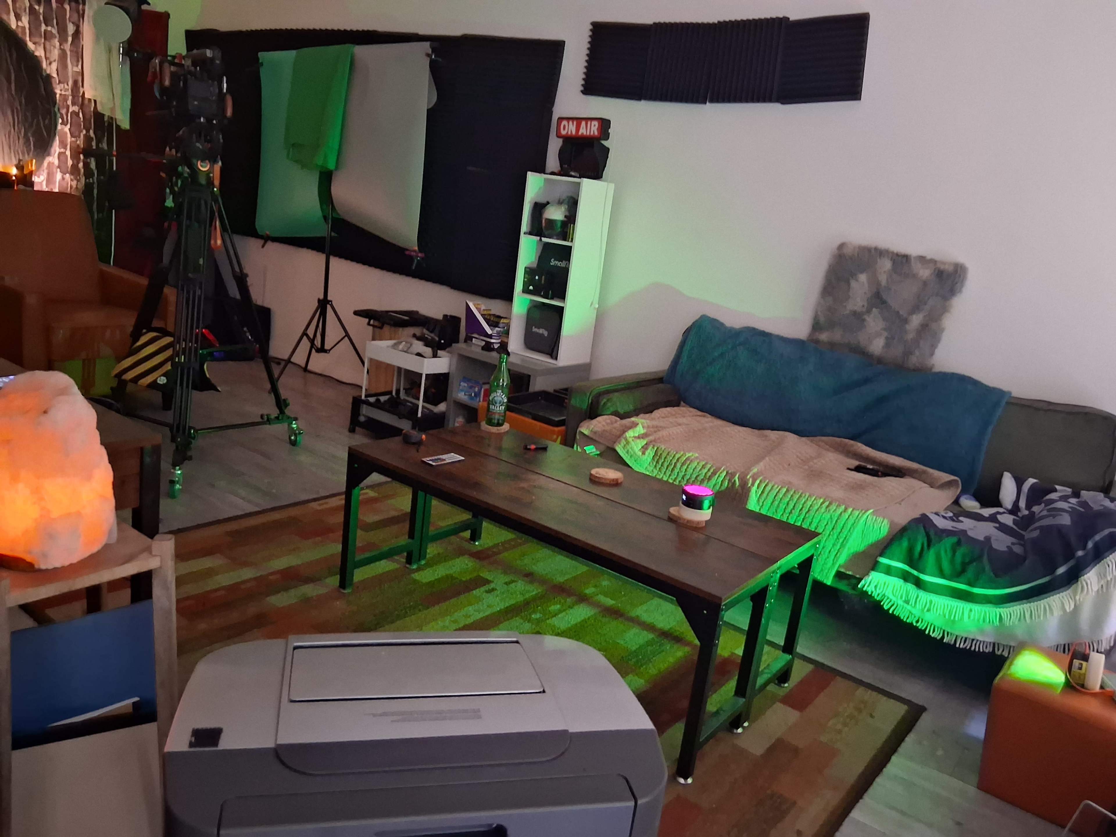 The image shows a multimedia studio setup with a couch, a table, and various filming equipment in the background.