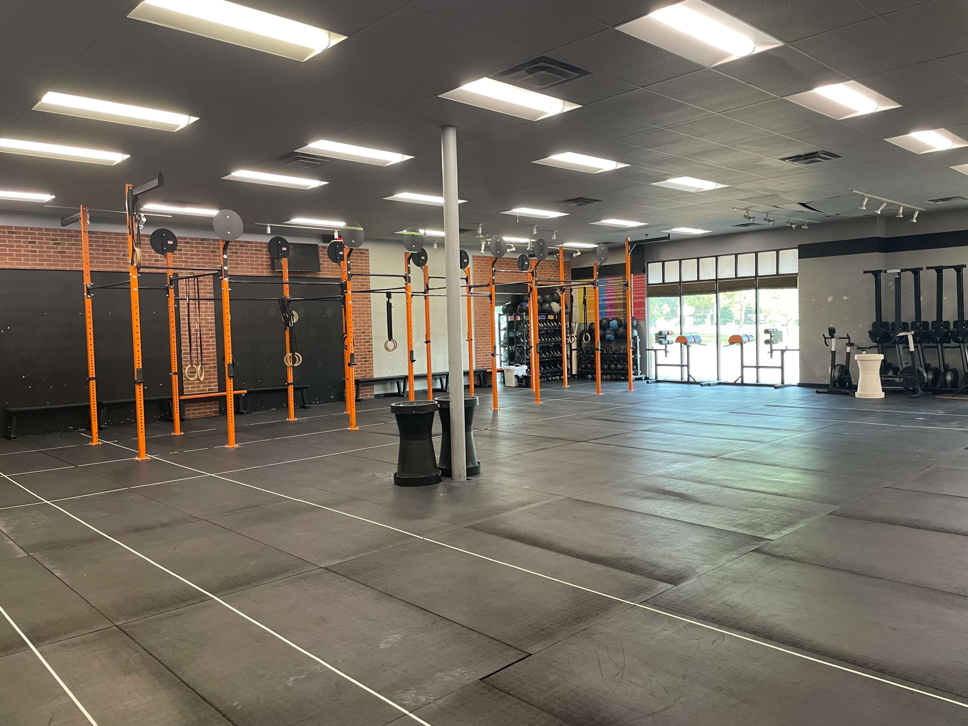 A spacious gym with orange pull-up bars and equipment arranged on black rubber flooring.