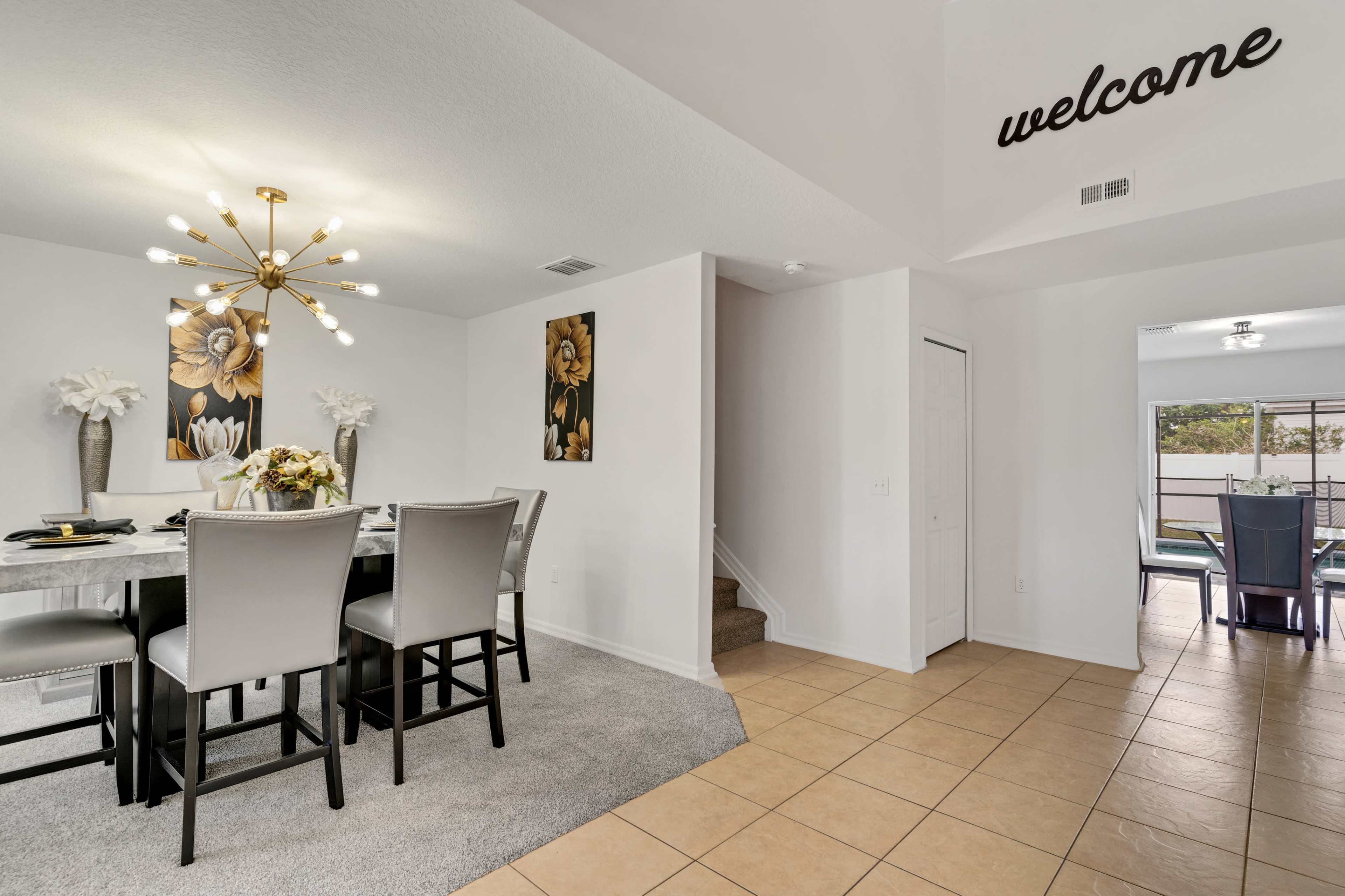 A dining area with a table set for a meal, framed floral wall art, and a welcoming message on the ceiling above.