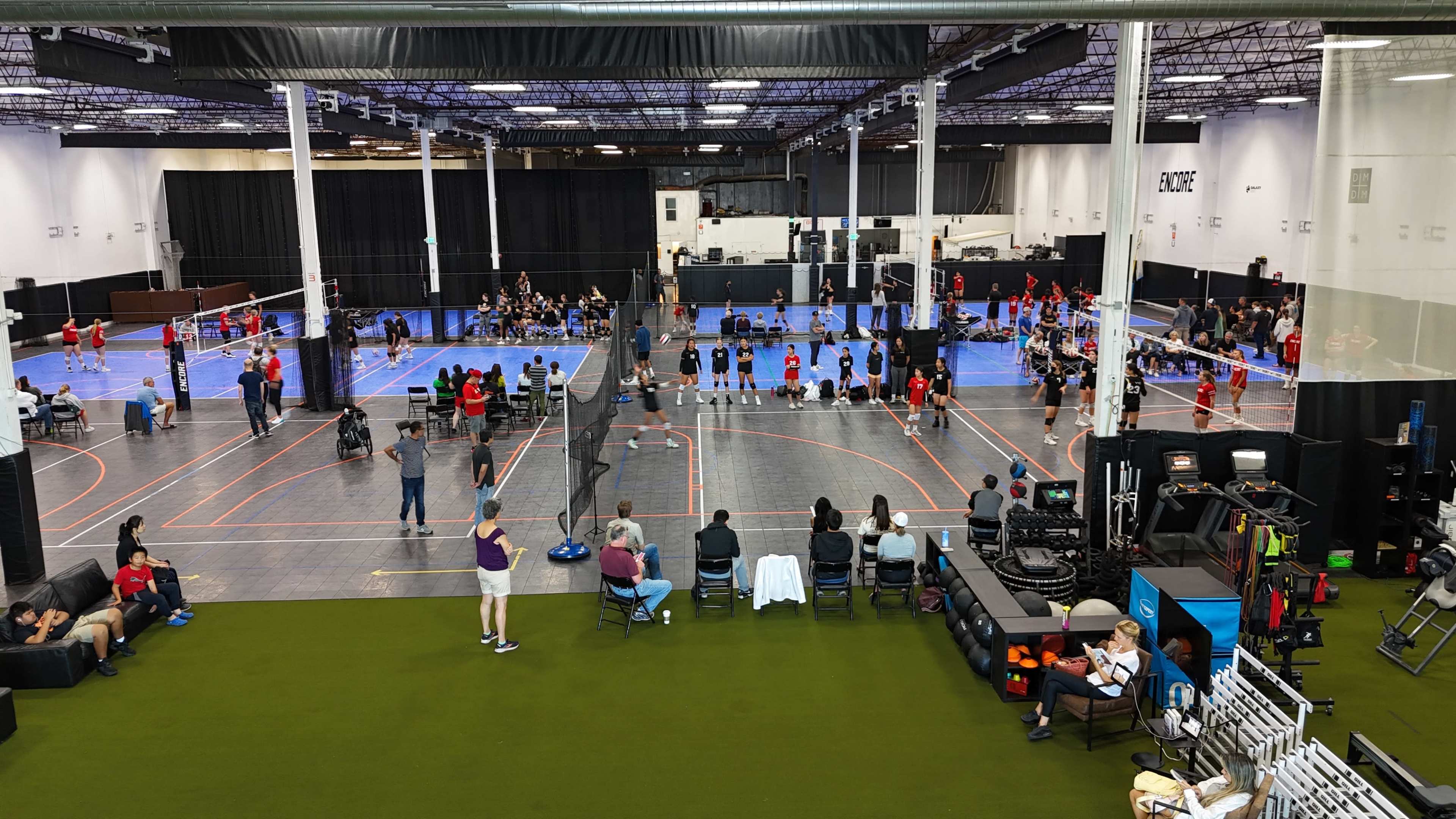 A large indoor sports facility with multiple volleyball courts, where teams are playing and spectators are seated.
